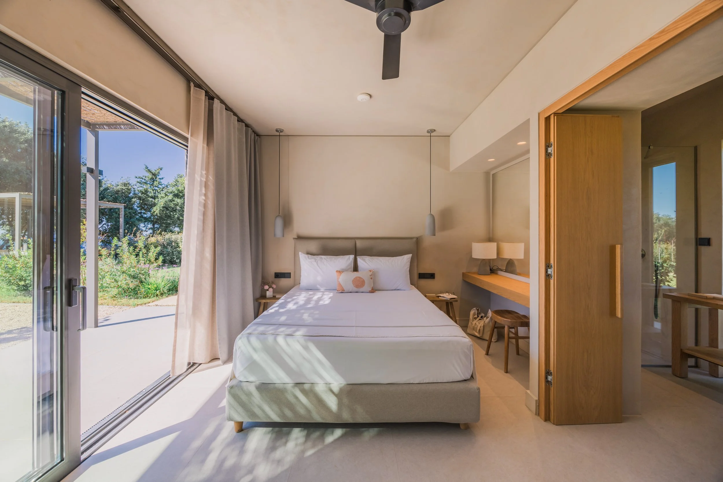 A hotel room with a bed, bedside tables, and a large glass door leading to an outdoor garden.