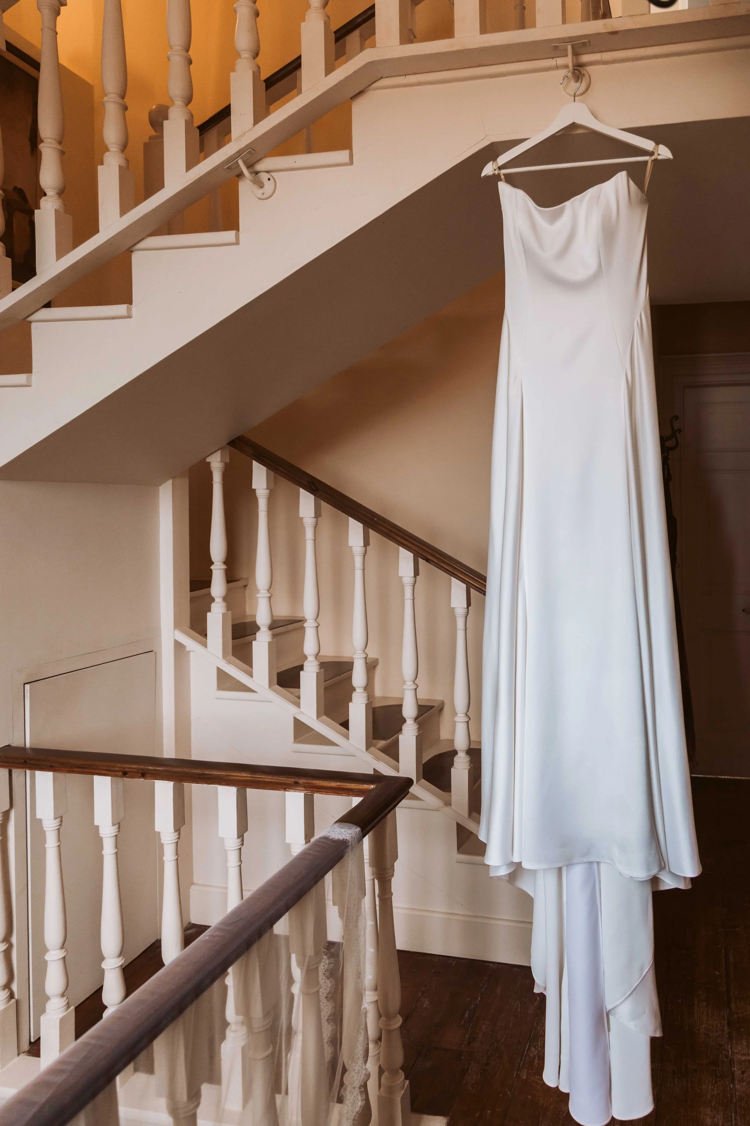 A white wedding dress hanging on a hanger on a staircase railing.