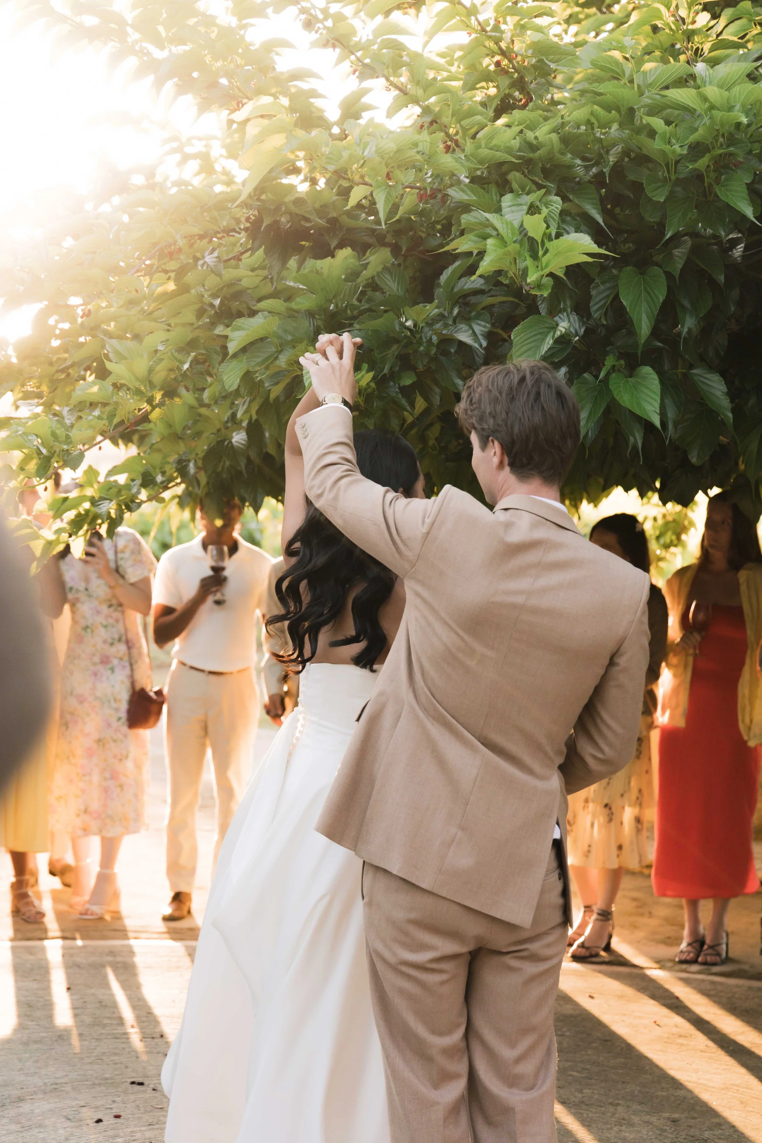 Couple dancing at an outdoor wedding ceremony during sunset with guests watching.