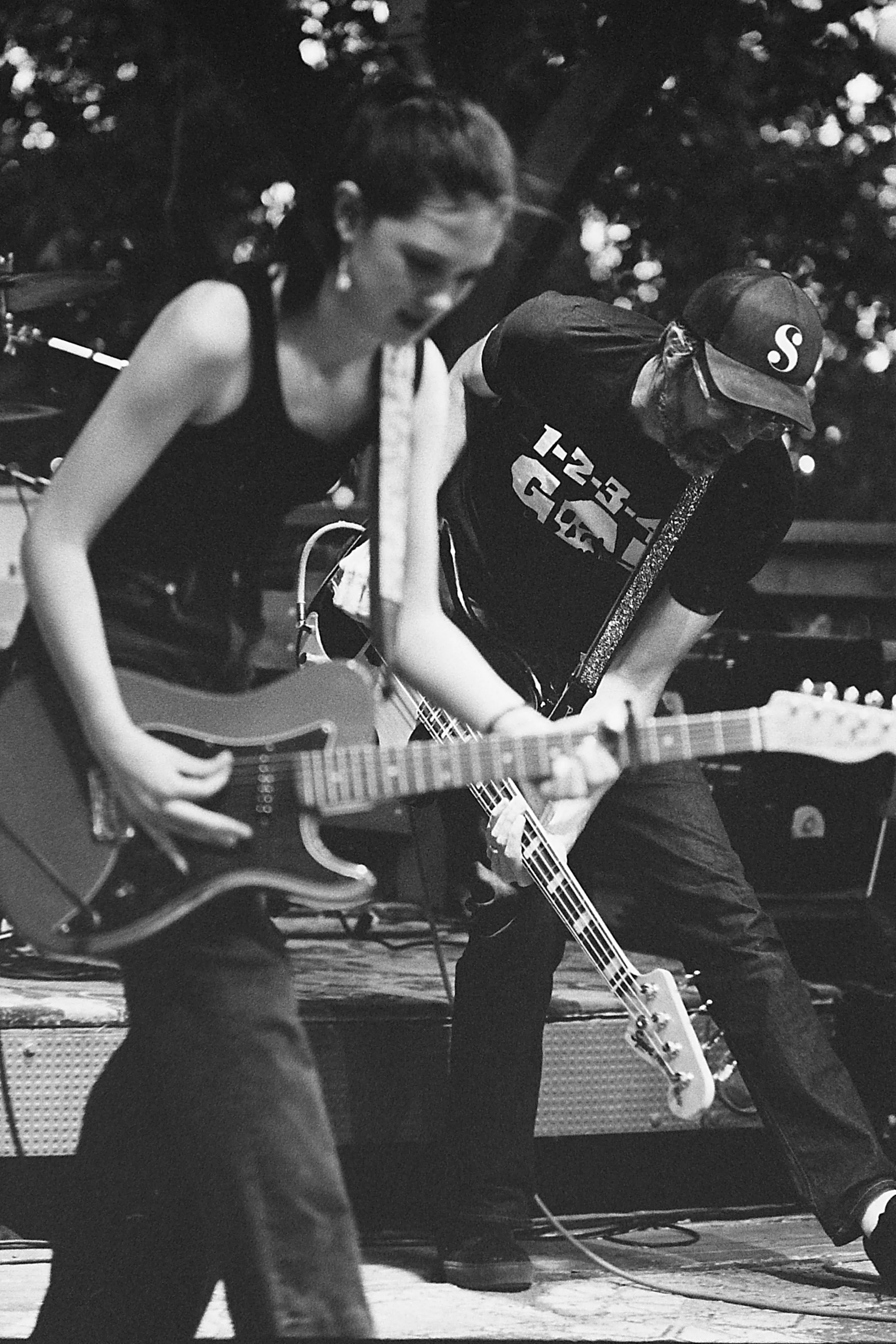 Two musicians, a woman and a man, performing with guitars on stage, with a dark background.