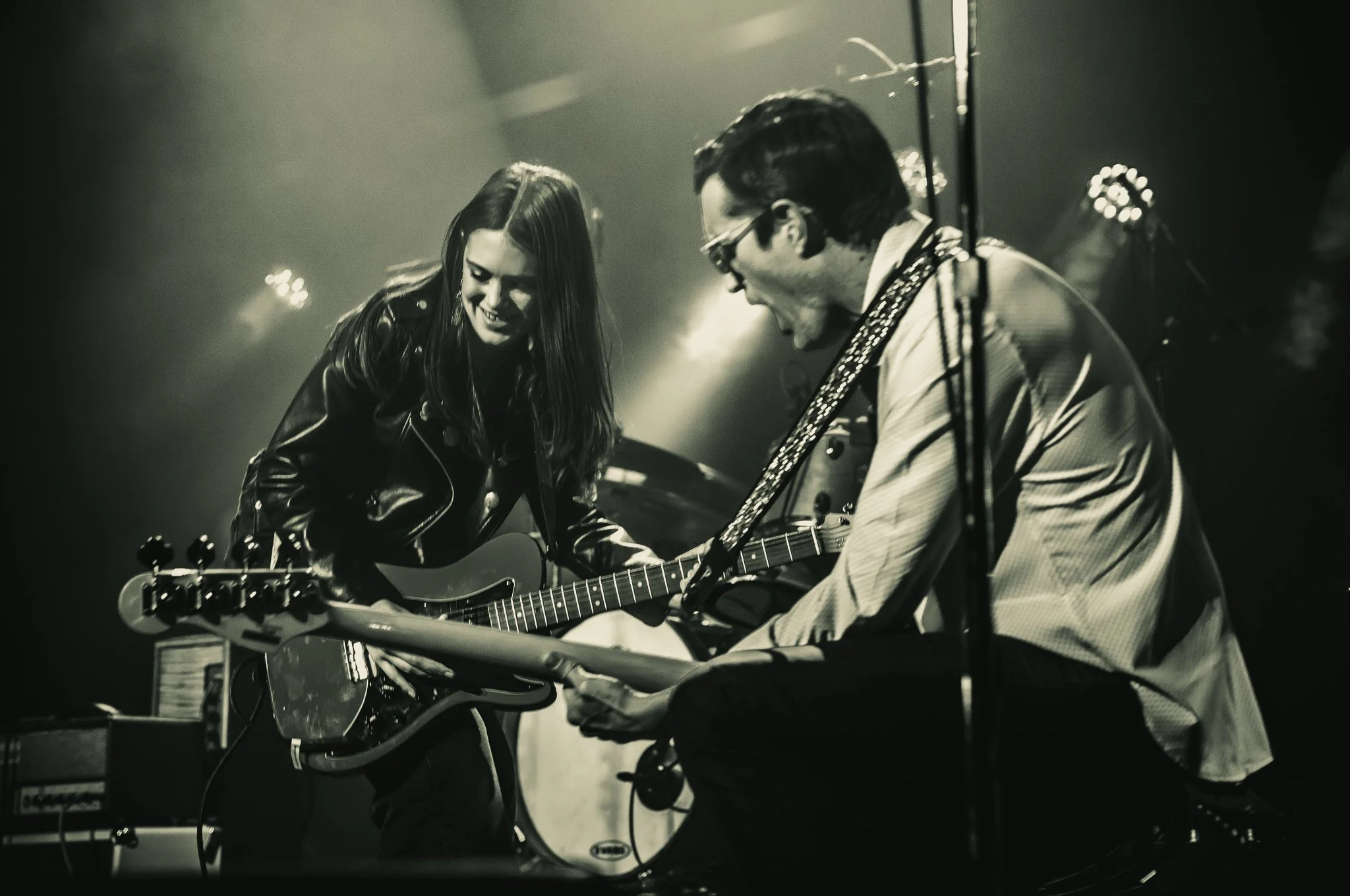 A woman and a man playing guitars during a live performance, smiling and enjoying each other's company.