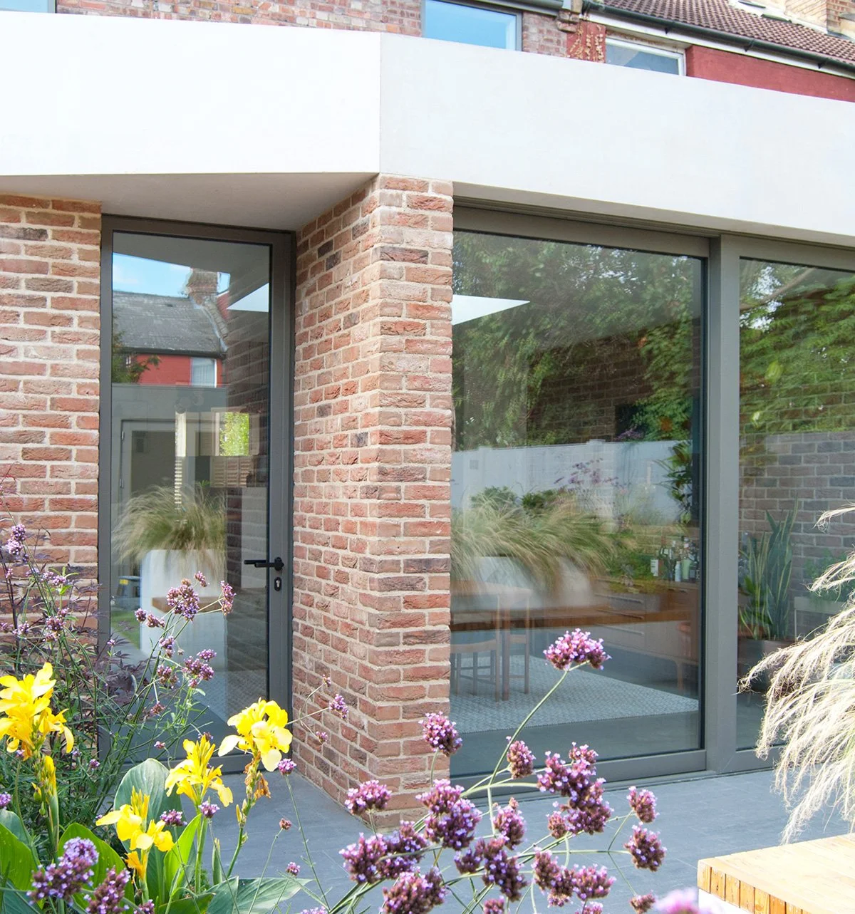Contemporary private garden with colourful perennial planting and a modern brick house entrance.