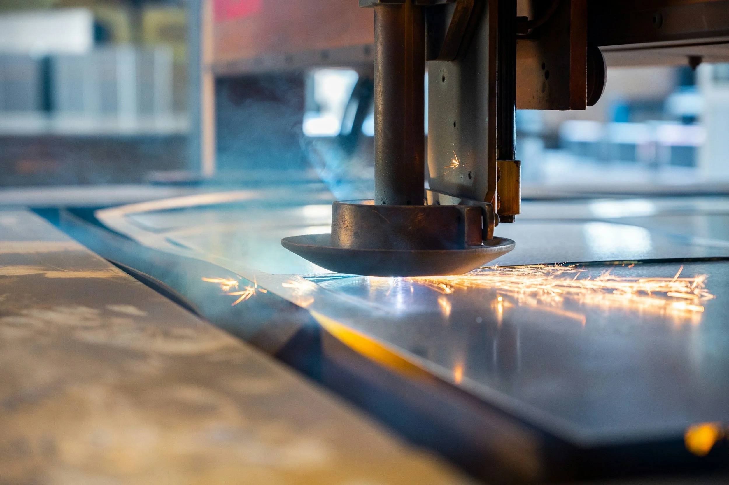 Close-up of a cutting machine performing laser or plasma cutting on a metal sheet, with sparks flying from the cut.