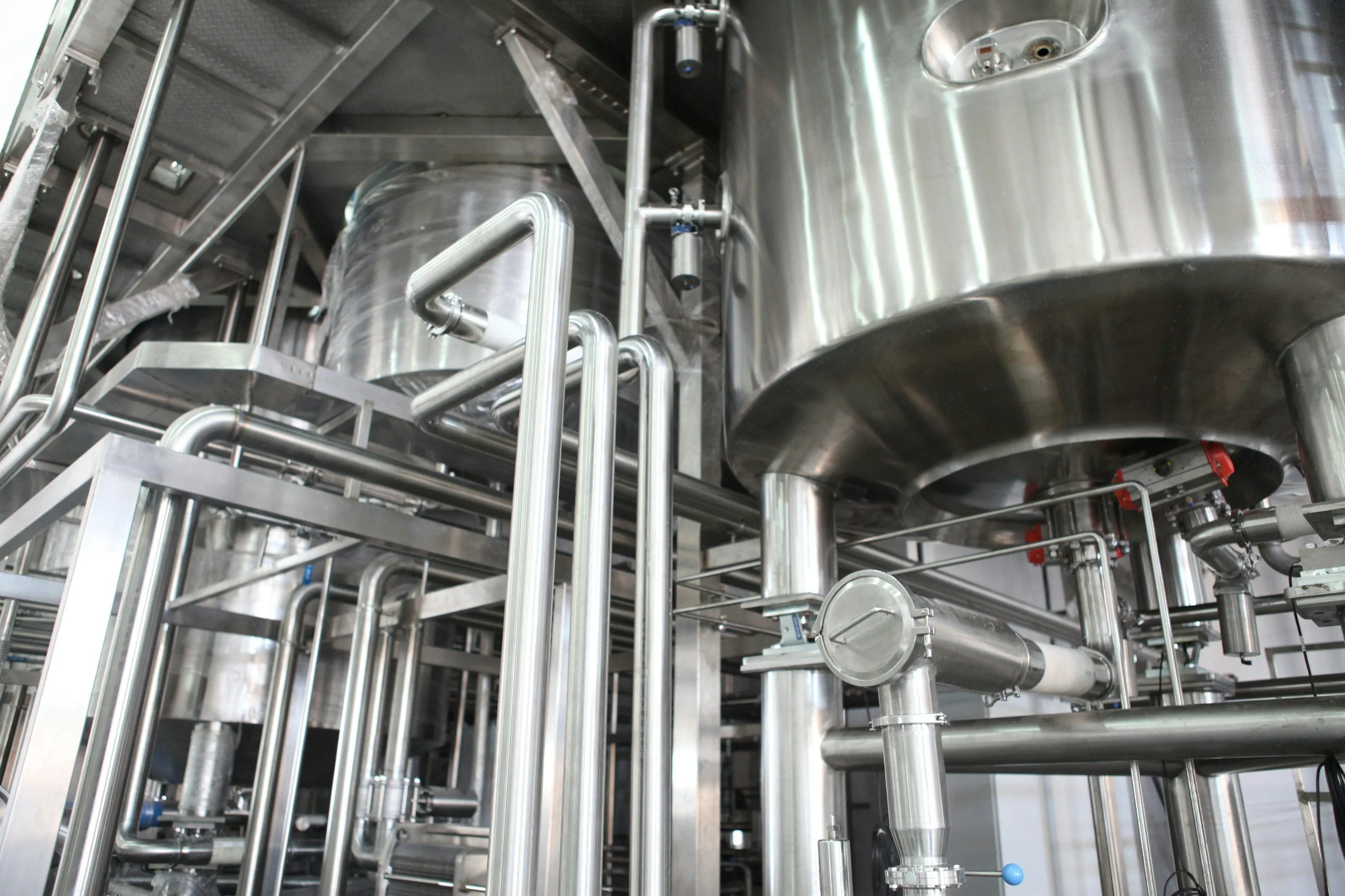 An industrial stainless steel processing setup with pipes, tanks, and valves, likely part of a manufacturing or chemical processing plant.