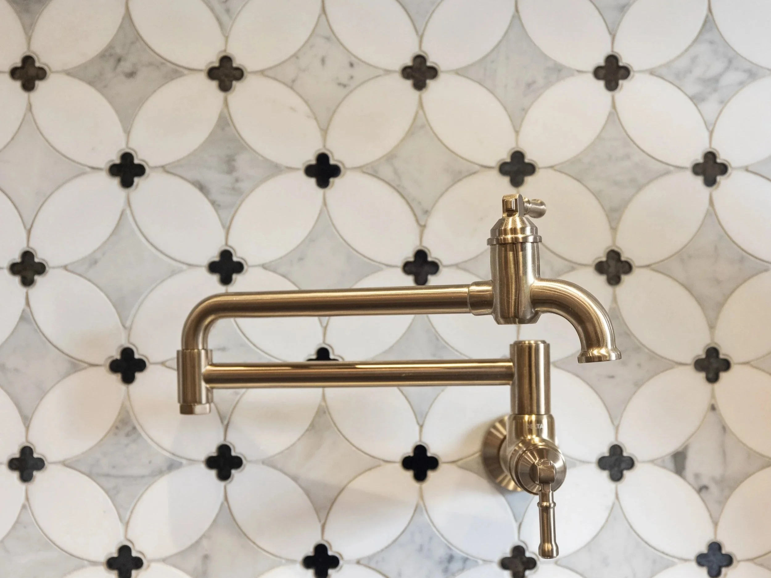 A renovated kitchen stove tile backsplash with a brushed silver wall-mounted pot filler. 