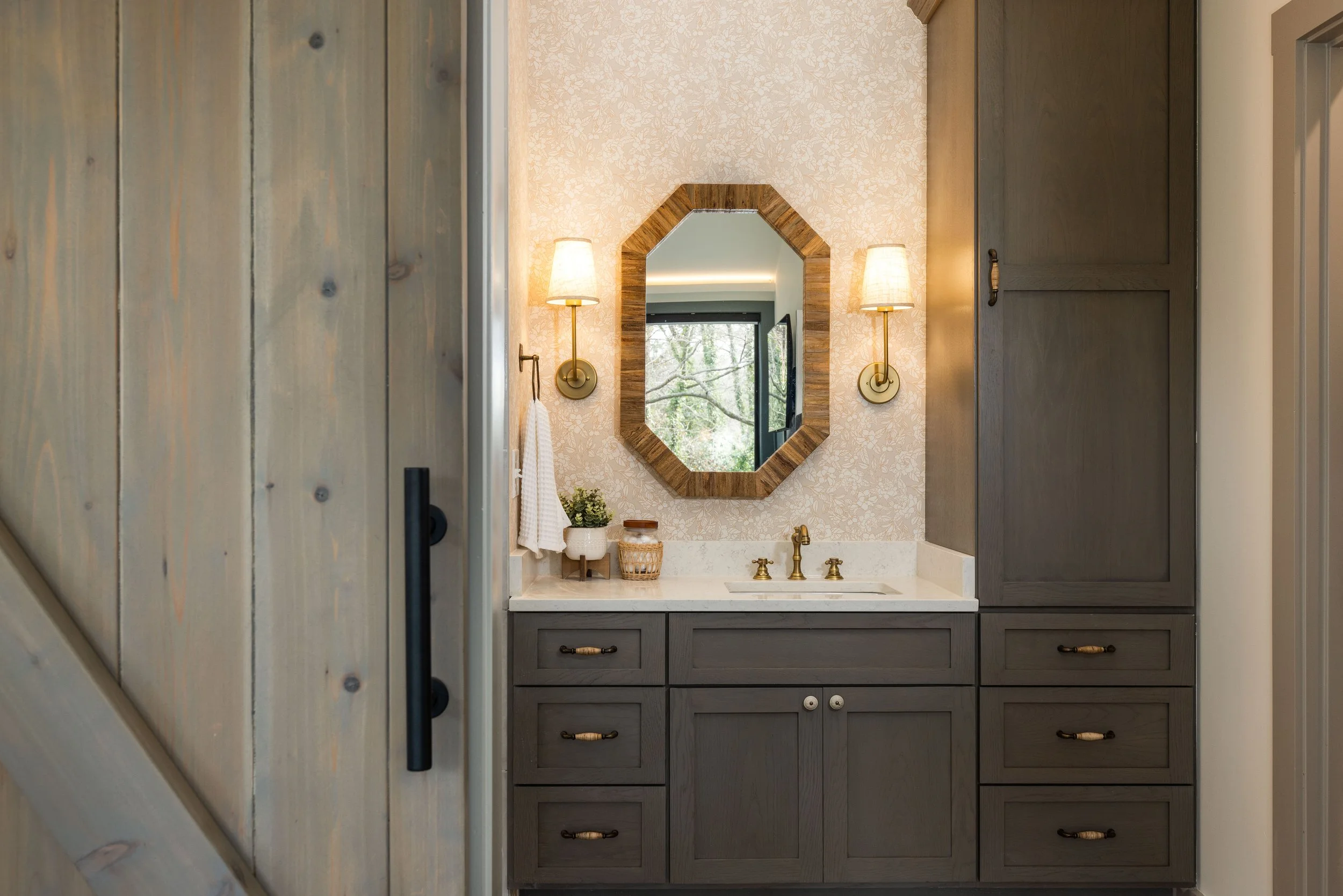 Bathroom vanity area with gray cabinets, a beige countertop, a mirror with a wooden frame, and wall-mounted lights on either side.