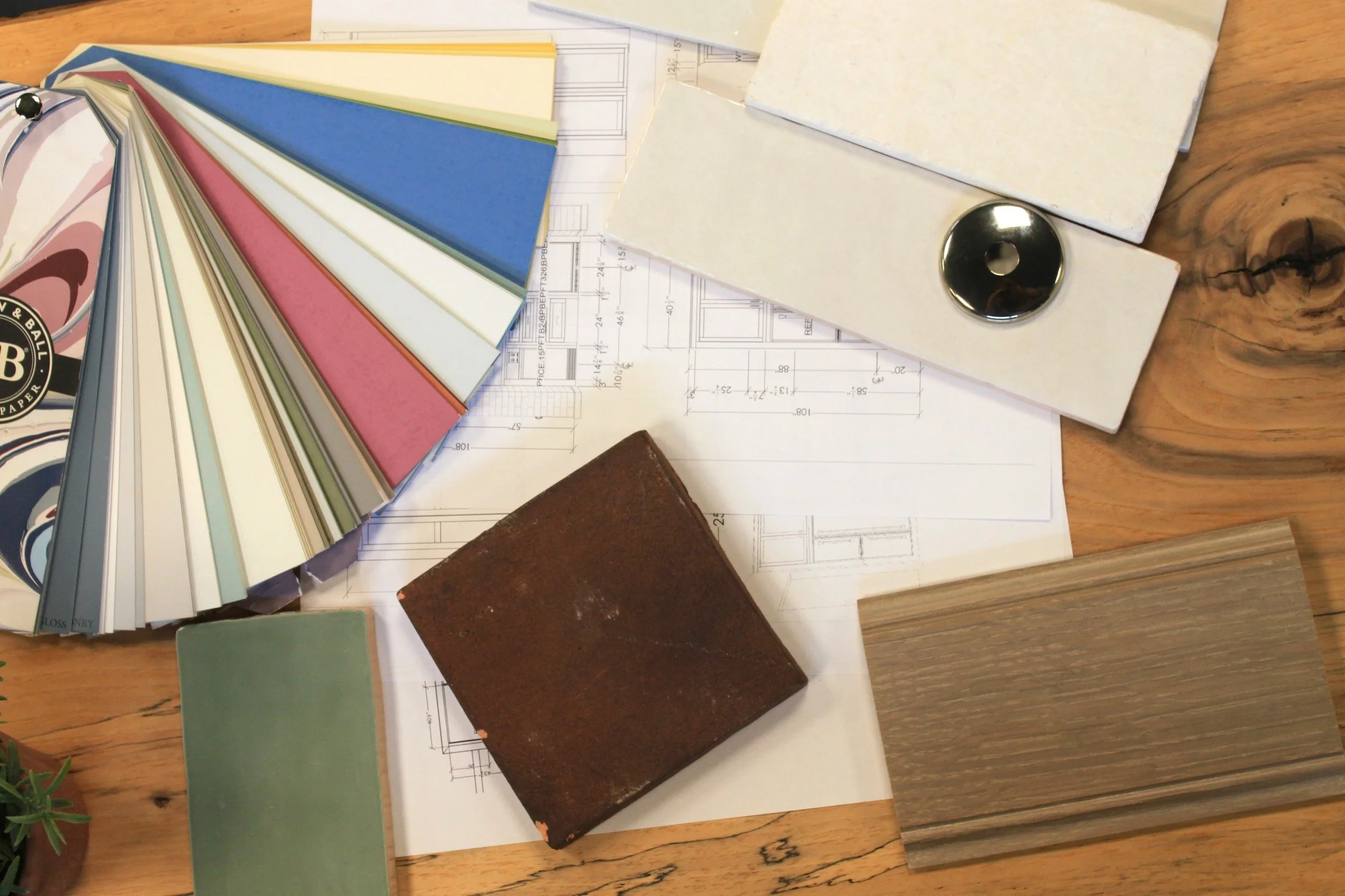 Various color sample fan deck, paint color swatches, fabric samples, and architectural blueprints on a wooden surface.