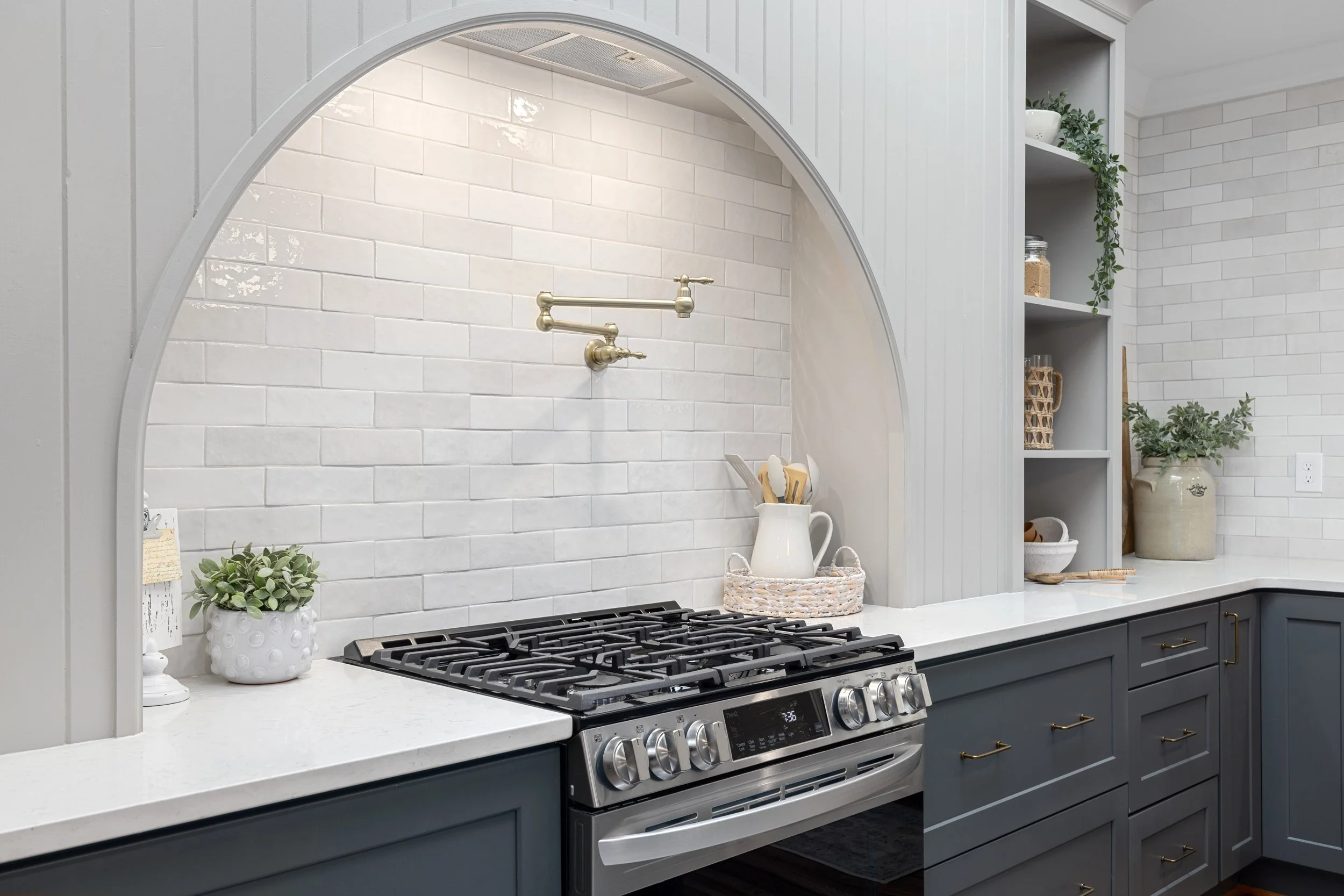 A kitchen renovation in Greenville, South Carolina with an arch above the stove range and white textured backsplash tile. 