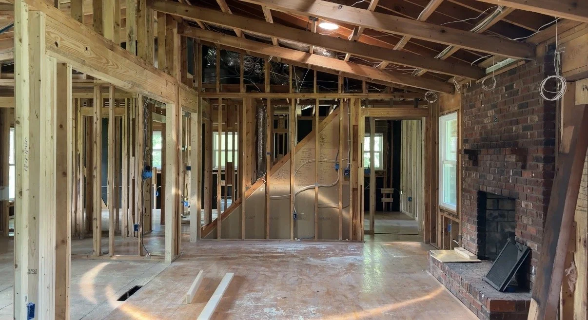 Interior of a house under construction with exposed wooden framing, electrical wiring, and a brick fireplace.