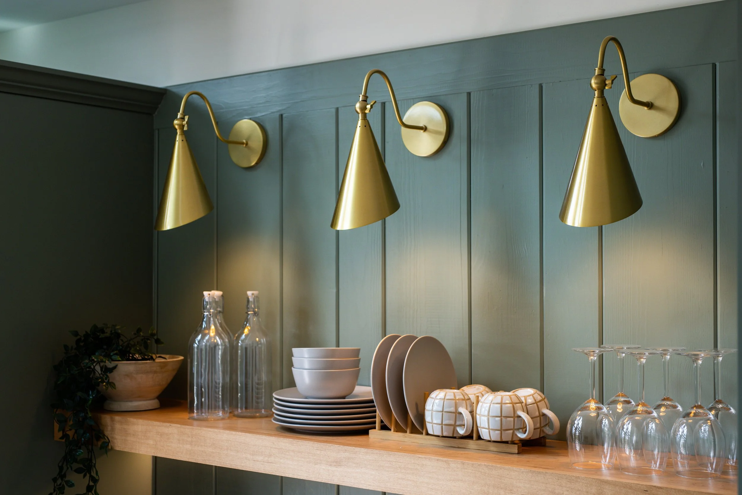 A renovated kitchen shelf in Greenville South Carolina with green wood paneling and brushed gold lamps. 