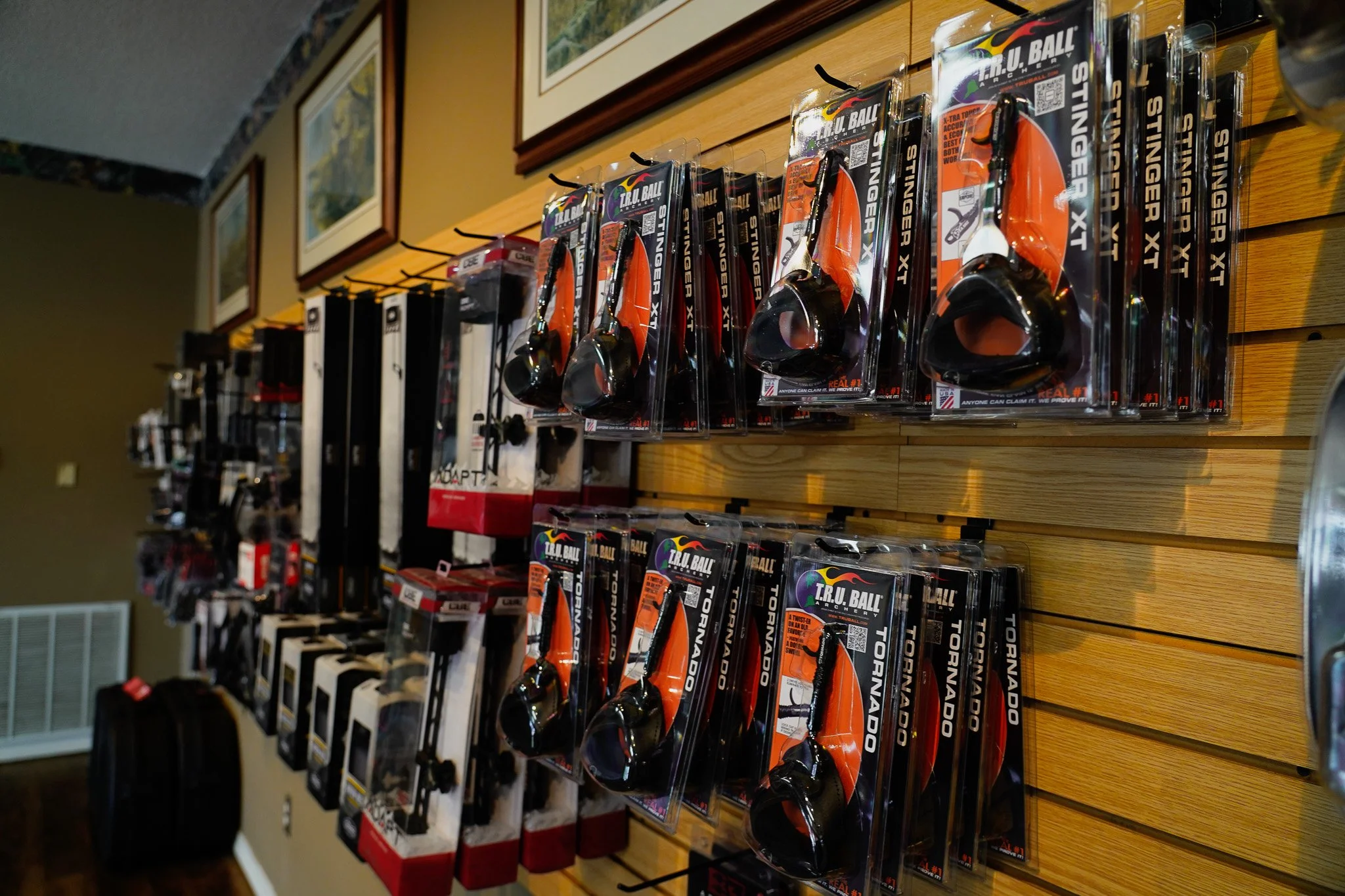 Display of archery equipment, specifically T.R.U. Ball archery releases, hanging on a wooden wall at a store.