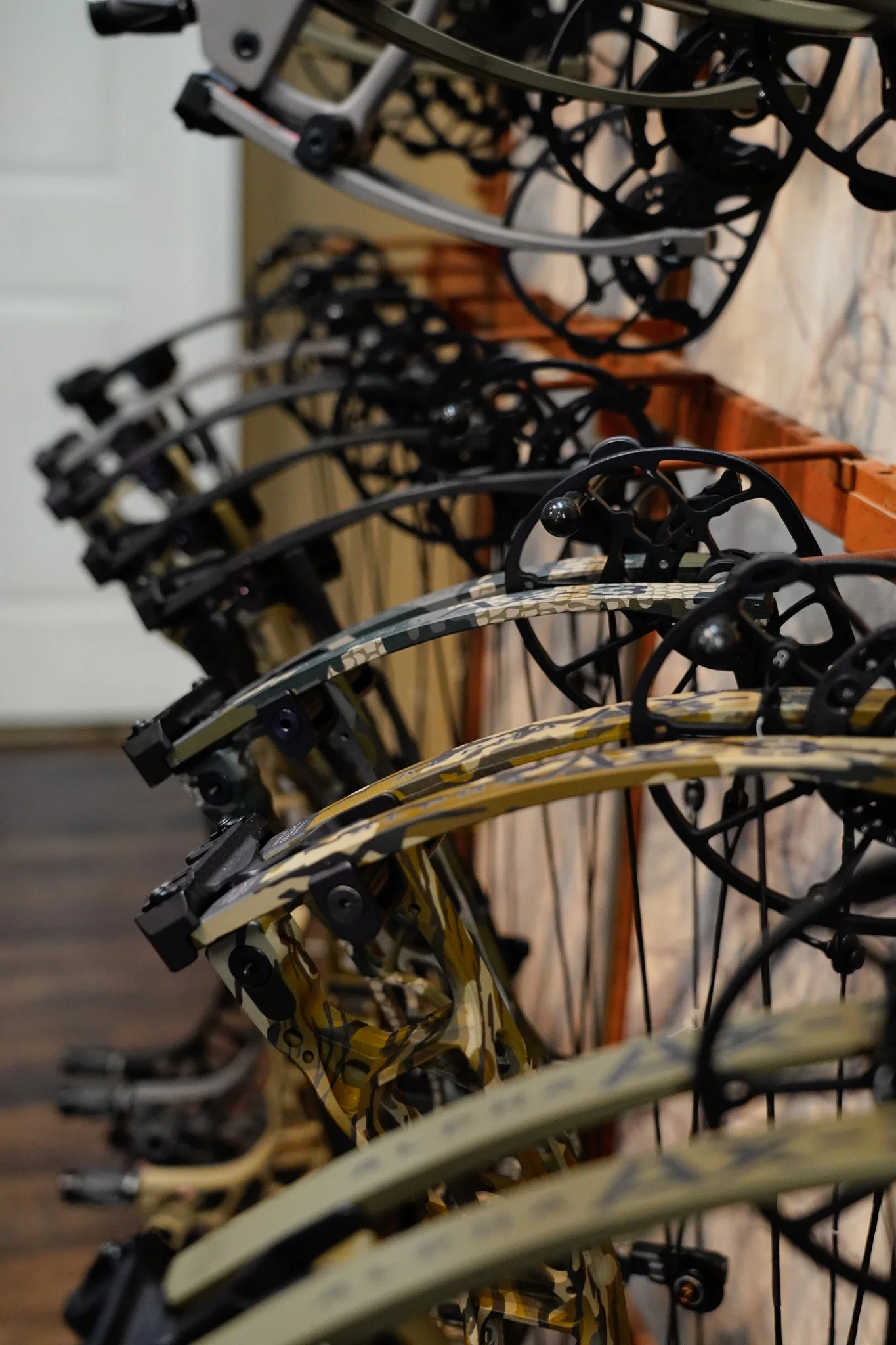Close-up view of a row of bicycle helmets with various patterns and colors, arranged on a metal rack indoors.