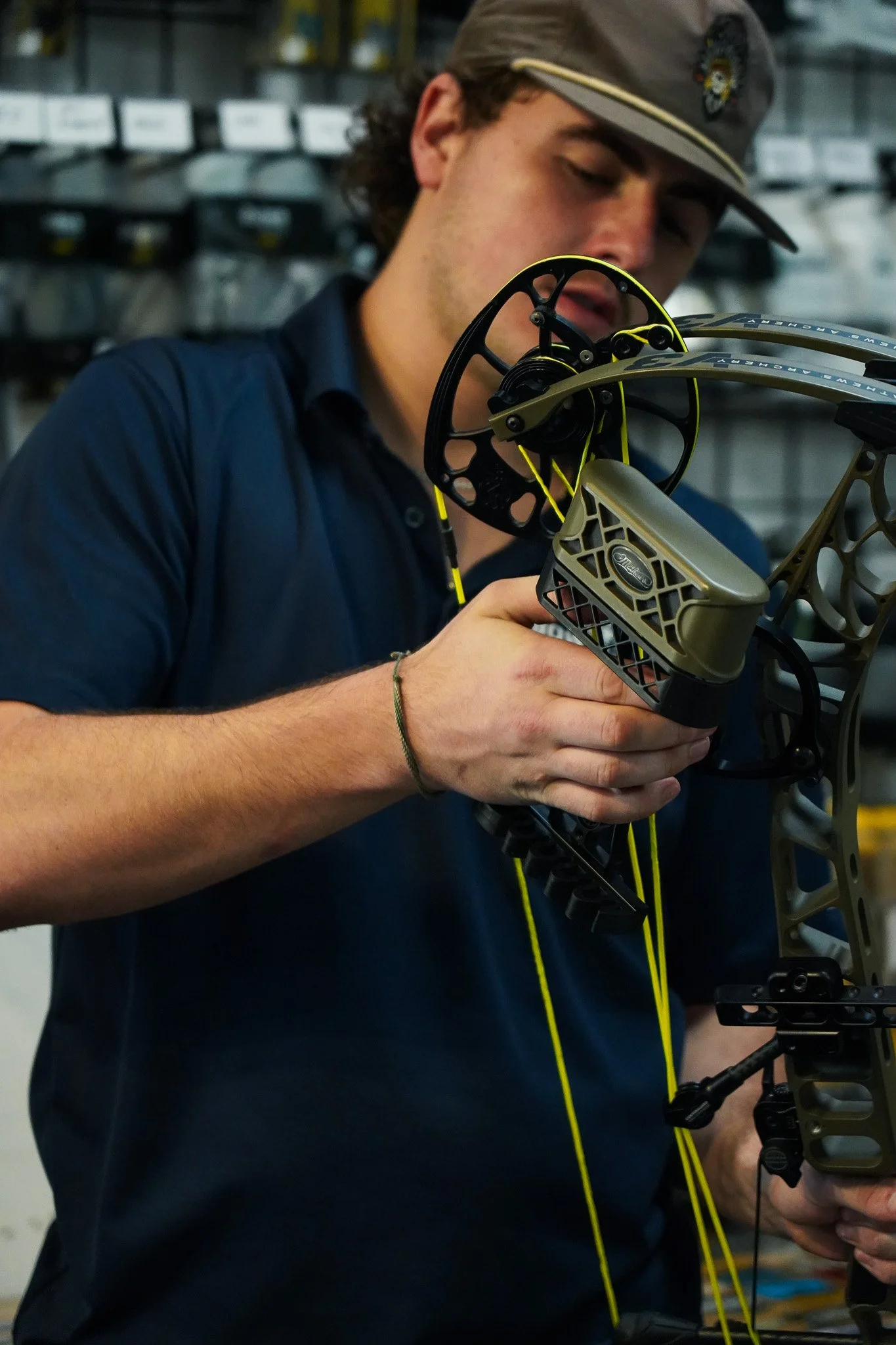 A young man inspecting a modern compound bow with a black and gold design in a store filled with archery equipment.