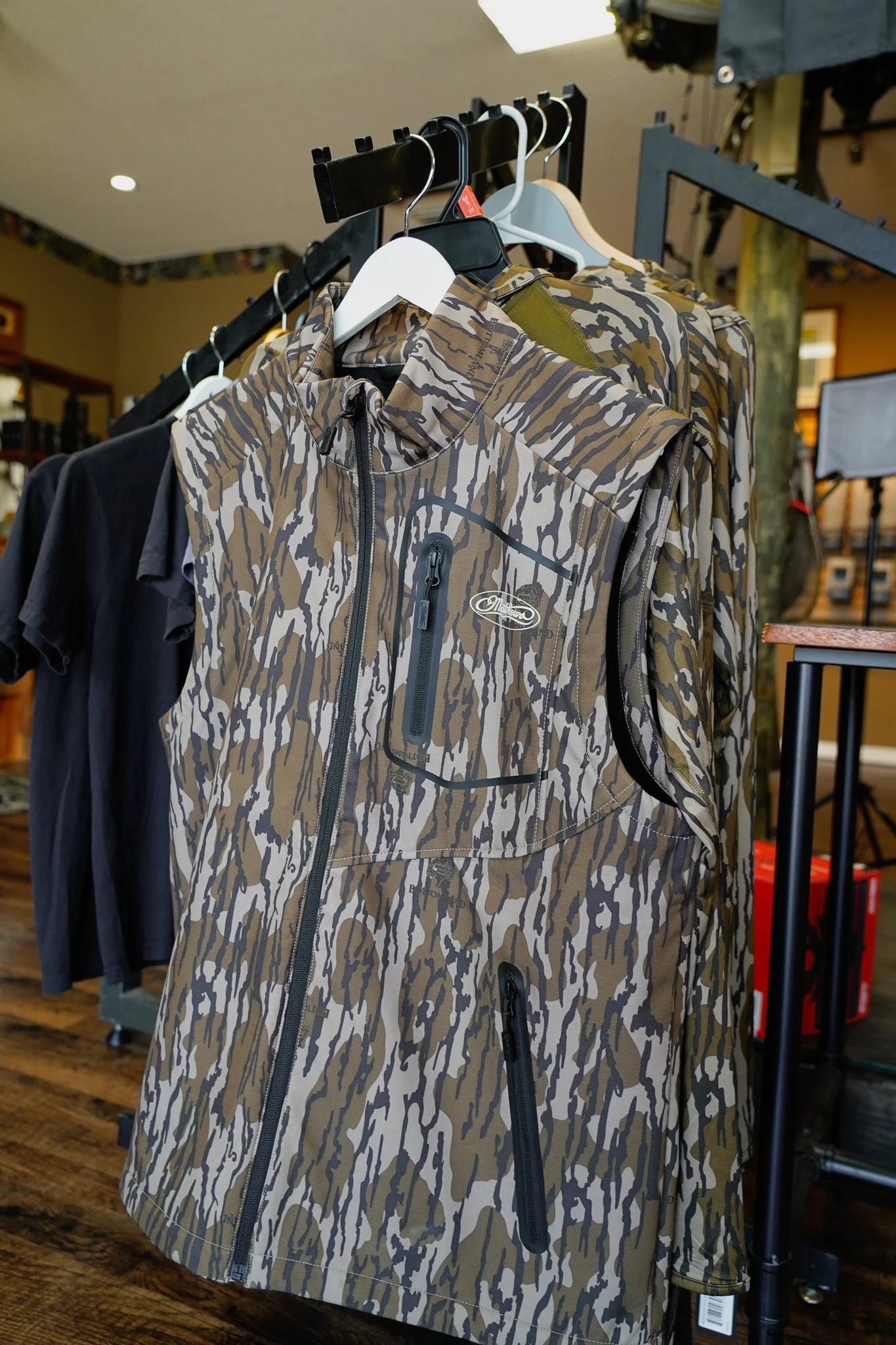 Multiple outdoor performance jackets hanging on clothing racks in a store, with one jacket featuring a camouflage pattern.