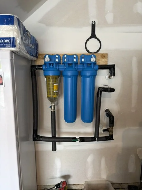Three-stage whole-home water filtration system with blue filter housings and black piping installed on a wall