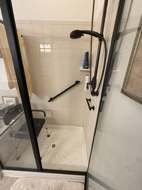 Walk-in shower with grab bars, a handheld shower head, and a small shelf
