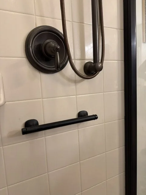 Accessible shower wall with a black grab bar, showerhead, and flexible hose