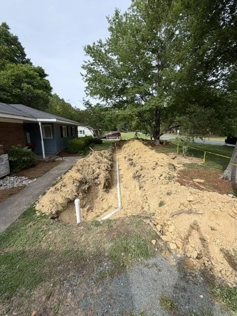 Yard excavation with exposed pipes and trenches near a house for a water service replacement