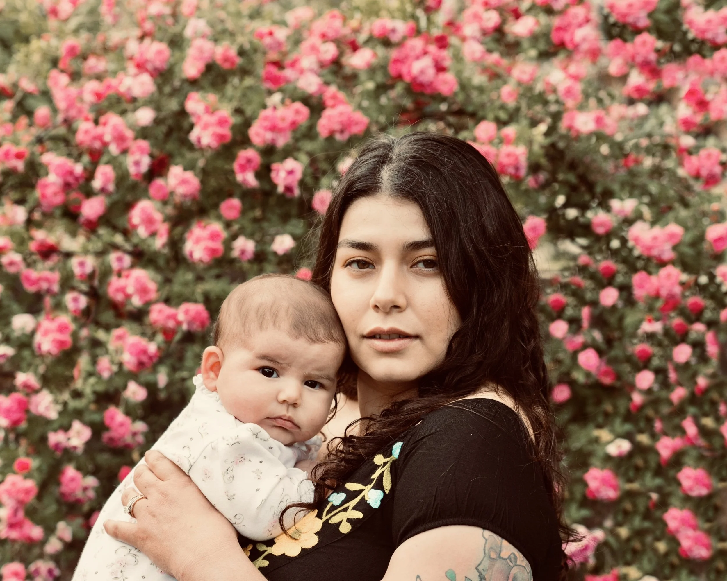 A woman holding a baby against a backdrop of pink roses.