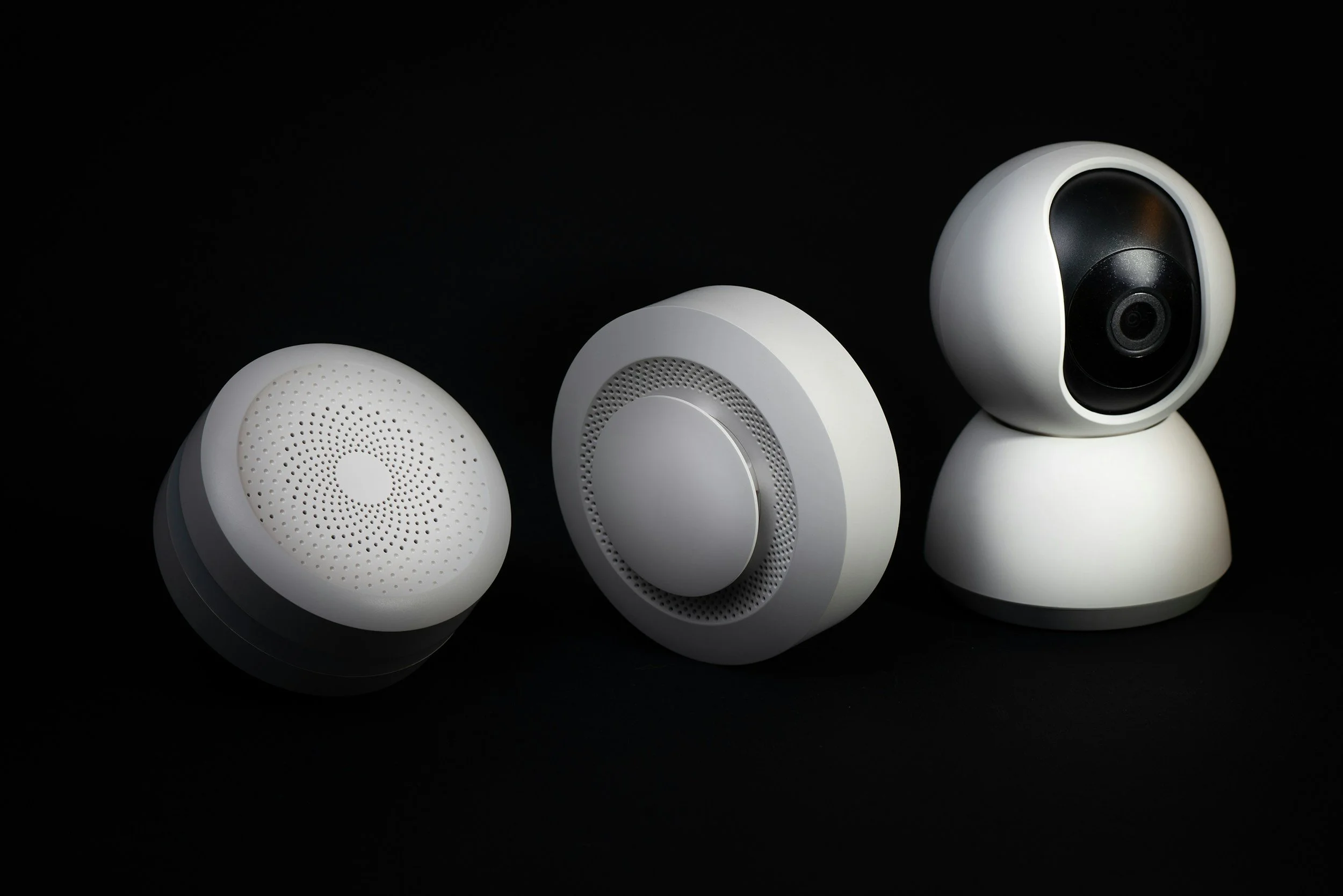 Three white security cameras or smart home cameras against a black background.