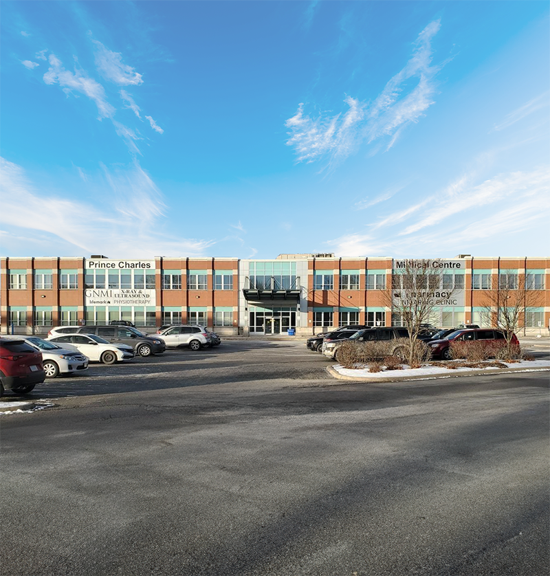 A large, two-story medical center building with a parking lot in front, under a blue sky with scattered clouds.