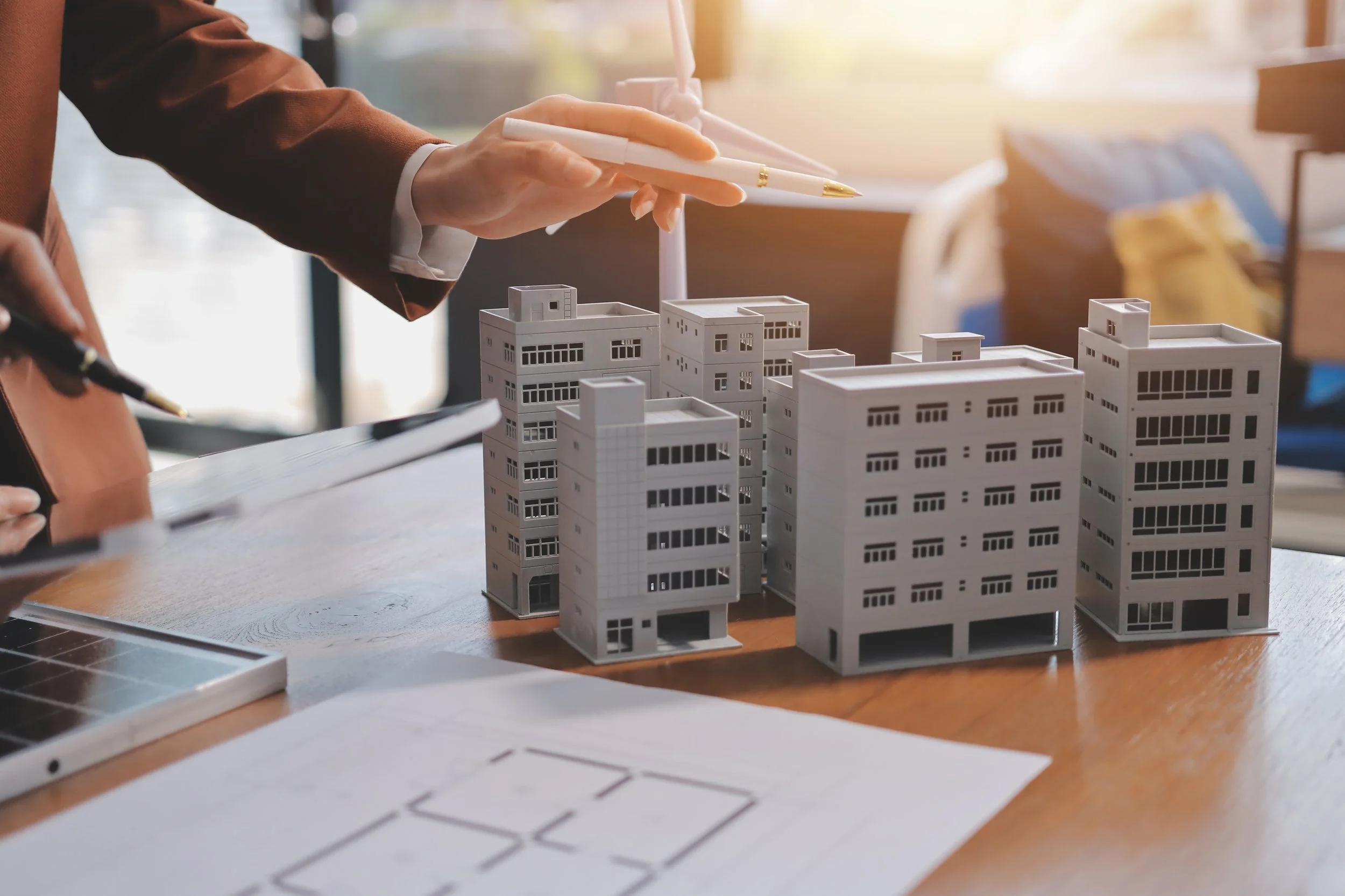 Person in a suit working on architectural models of buildings and city layouts on a desk.