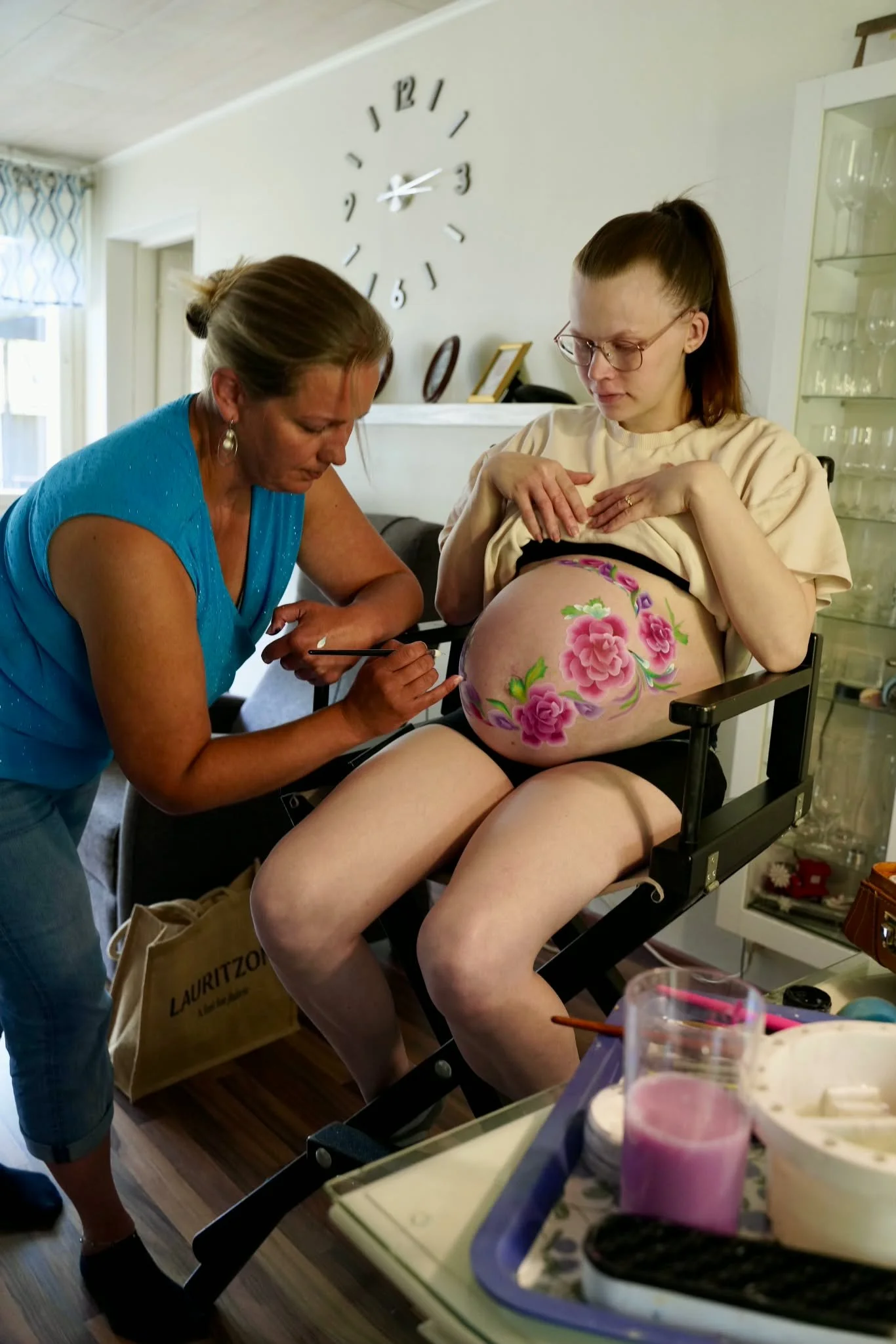 Mona Hyvärinen tekee raskausmahan maalausta aiheena kukat ja lapsen syntymän laskettuaika (päivämäärä)