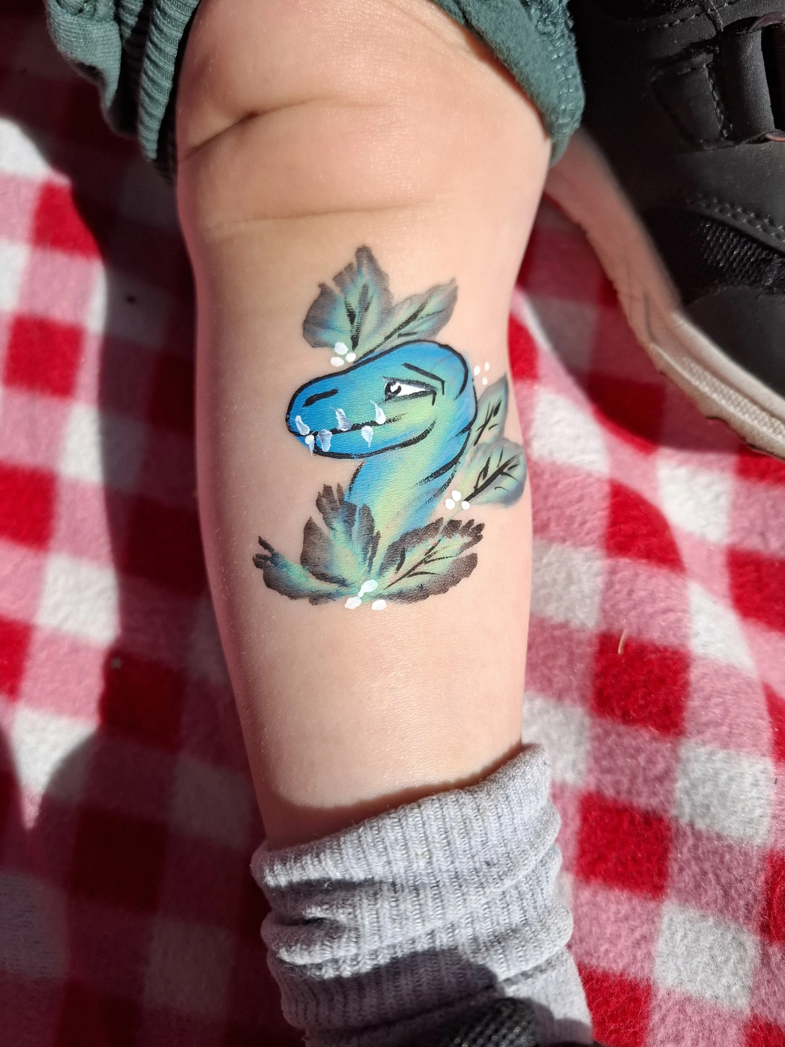 Ihomaalaus kädessä, jossa on pieni sininen dinosauruksen pää ja lehdet.