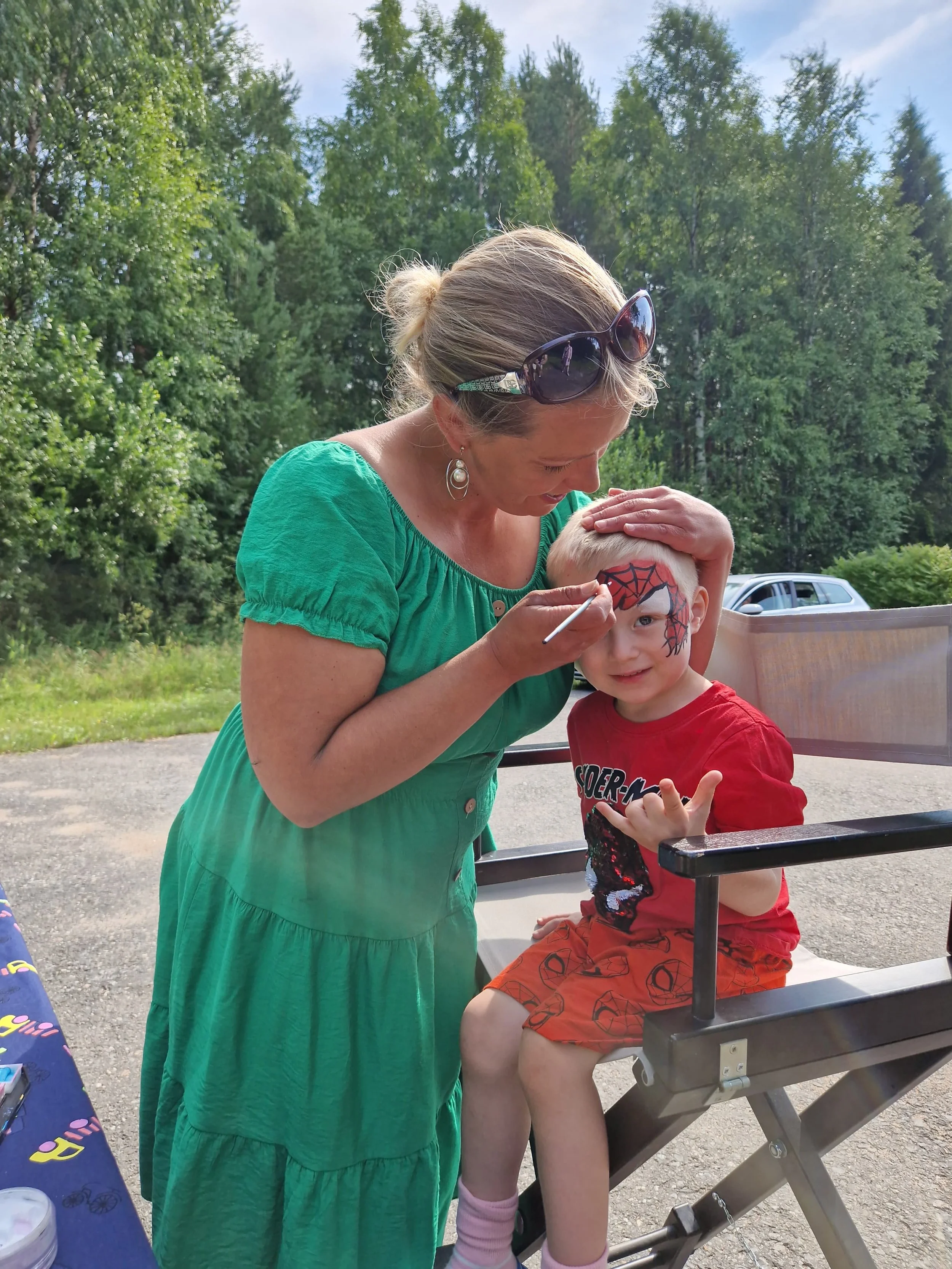 Nainen maalaamassa pikkupojan kasvoihin, kasvoihin on maalattu Spiderman-teema.
