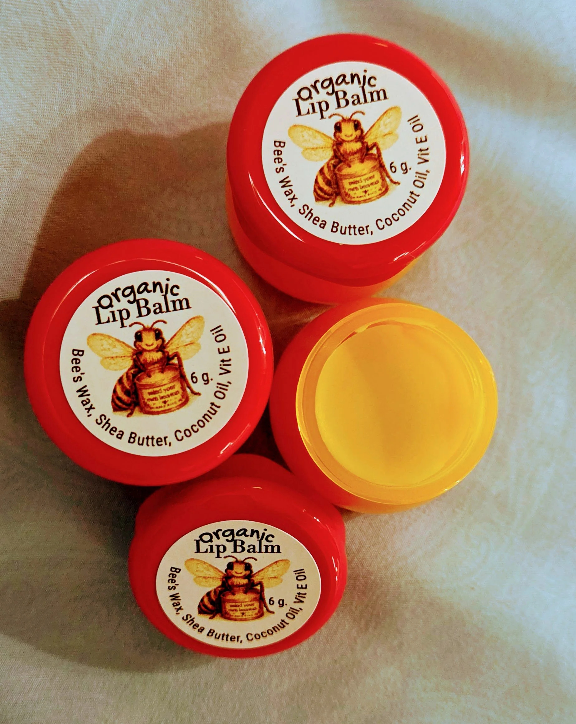 Mini honey-pot style containers of Mind Your Own Beeswax organic lip balm, with one open pot showing the golden organic lip balm inside.