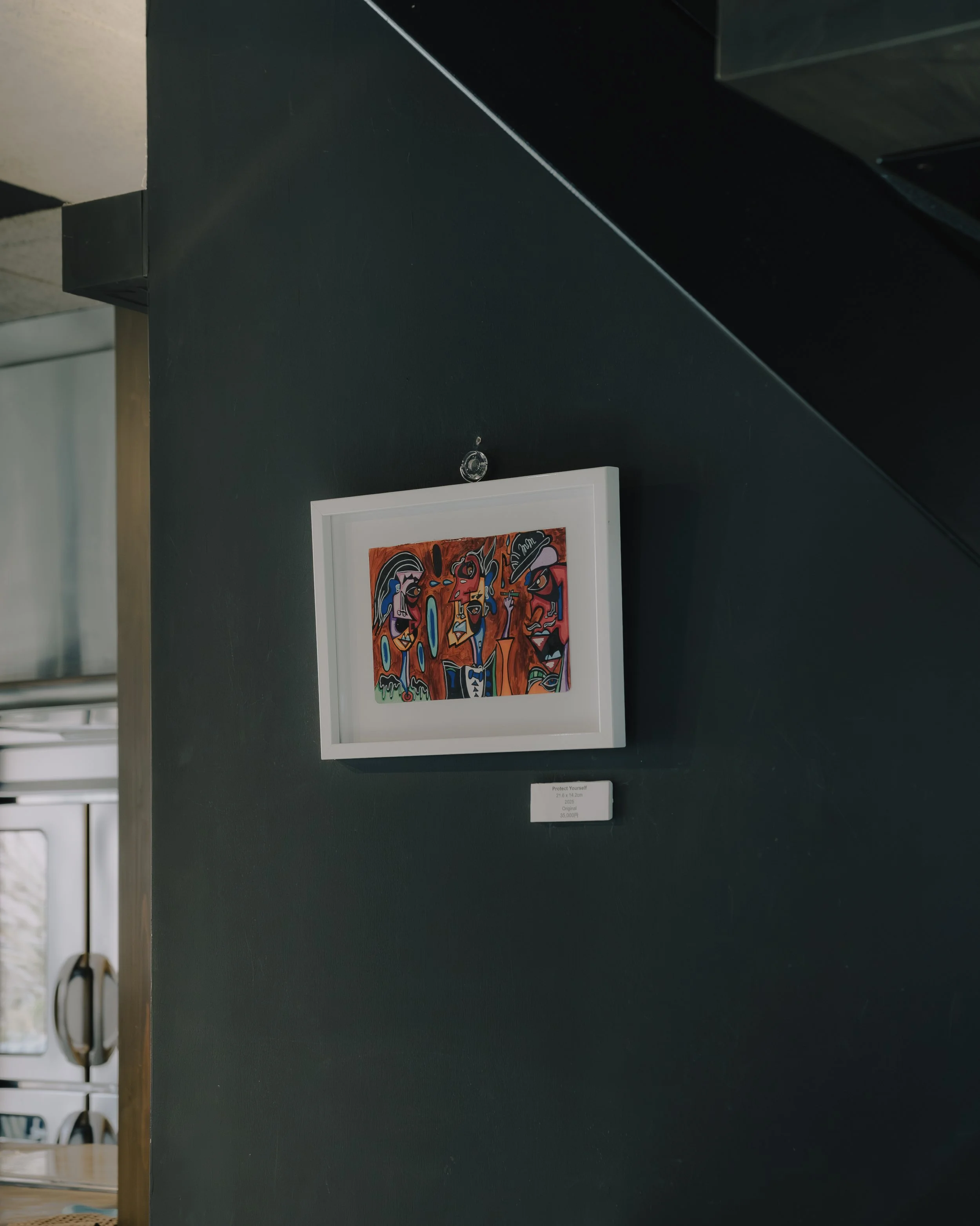 A colorful abstract painting in a white frame hanging on a dark wall, with a small label underneath detailing the artwork.
