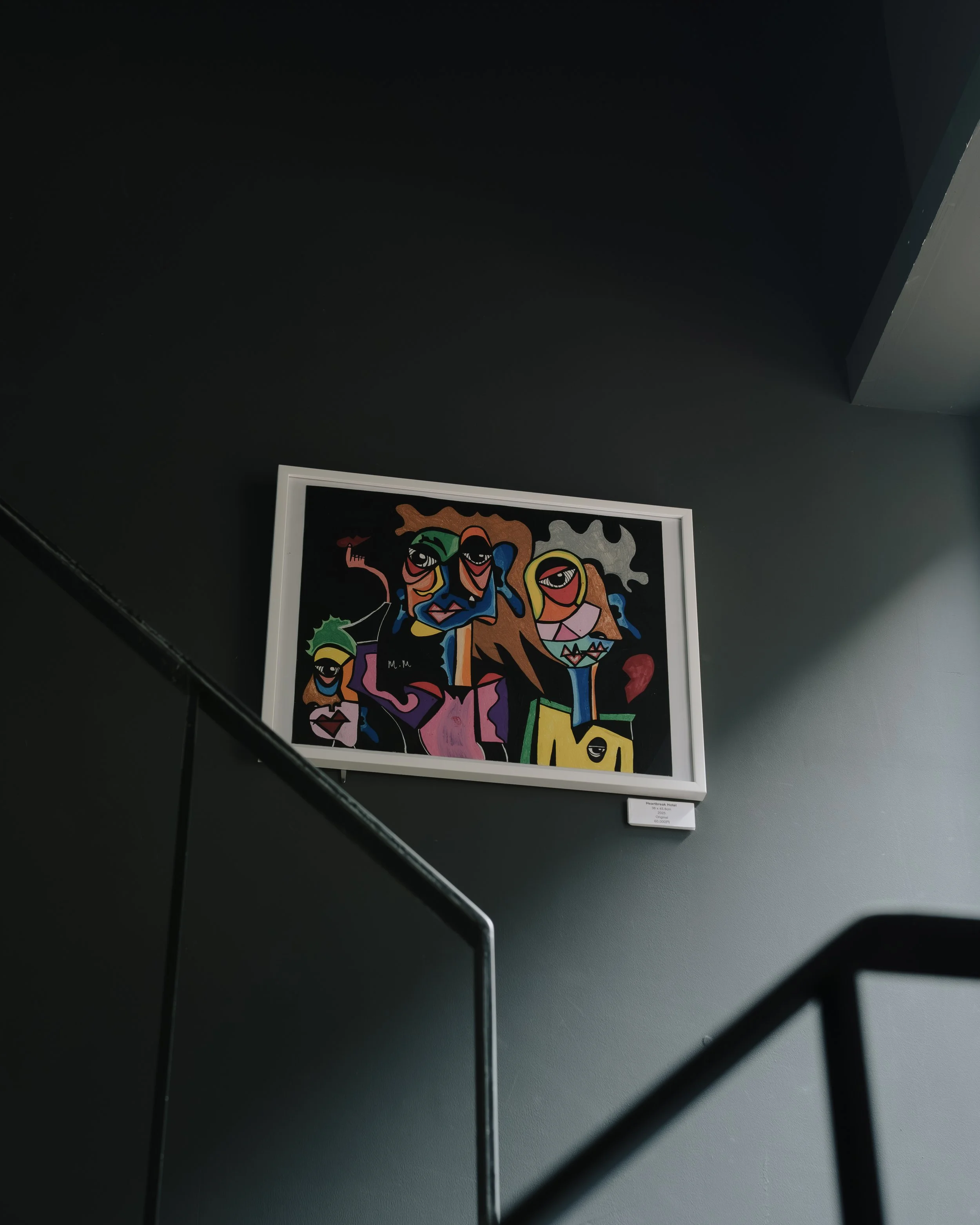 Colorful abstract artwork with faces and shapes in a white frame hung on a dark gray wall.
