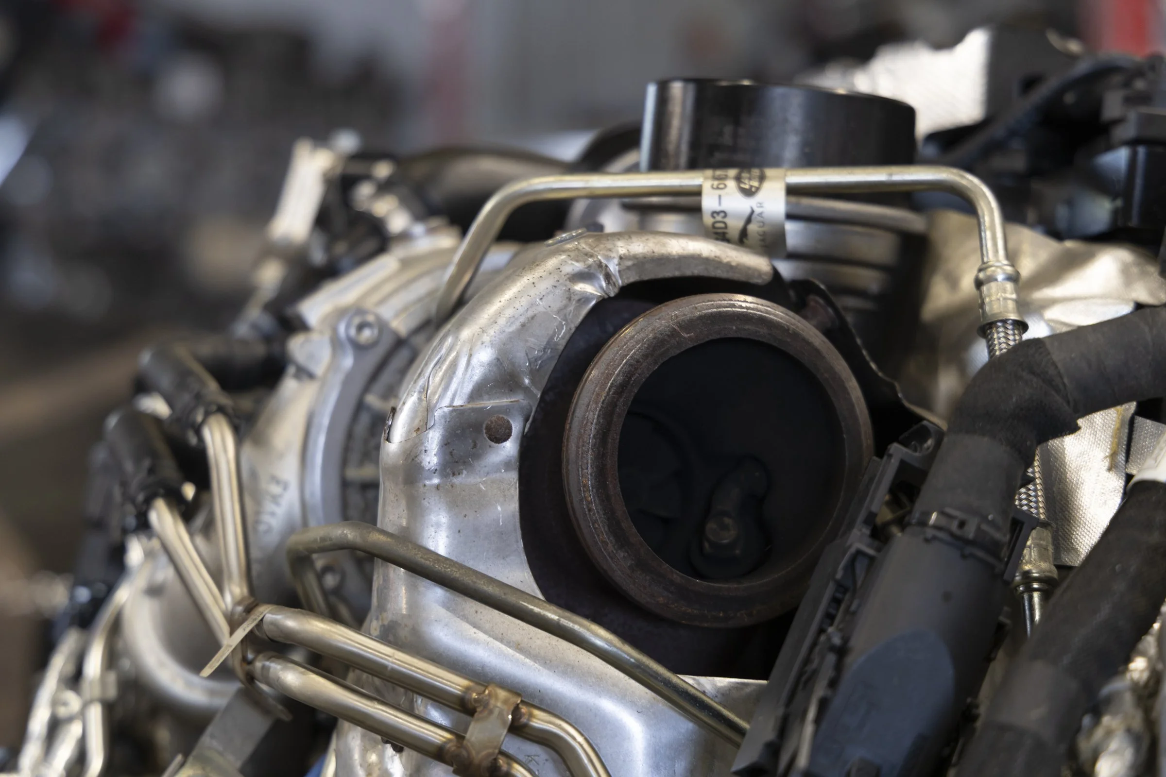 Close-up picture of a mechanical engine component with metallic parts and tubing, with a label attached