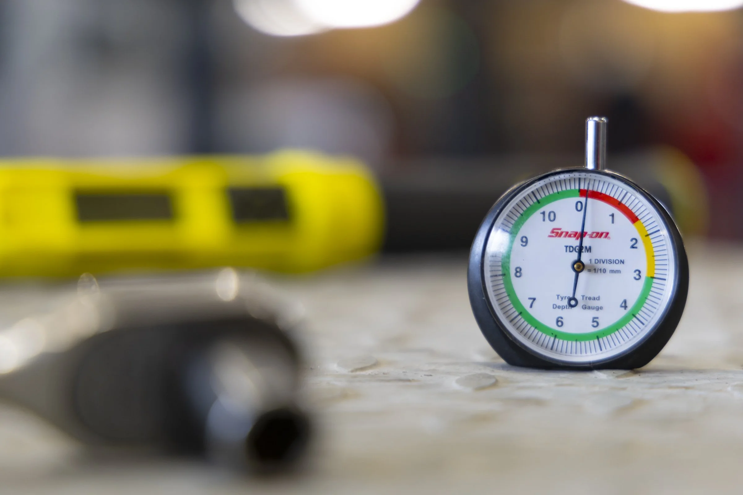 Close-up of a pressure gauge with a blurred yellow object in the background.