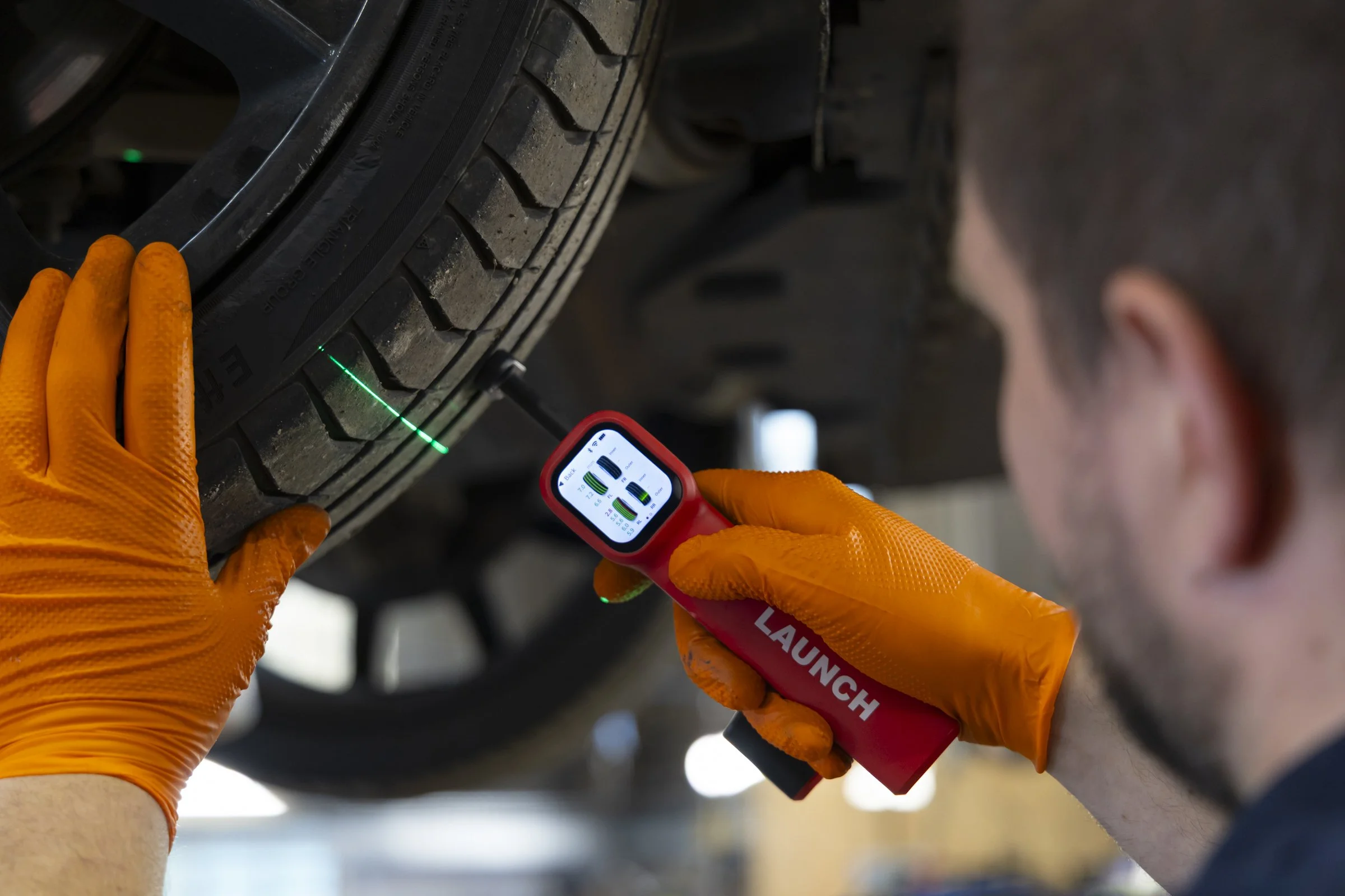 A person in orange gloves using a laser tool to measure tire tread depth on a vehicle.
