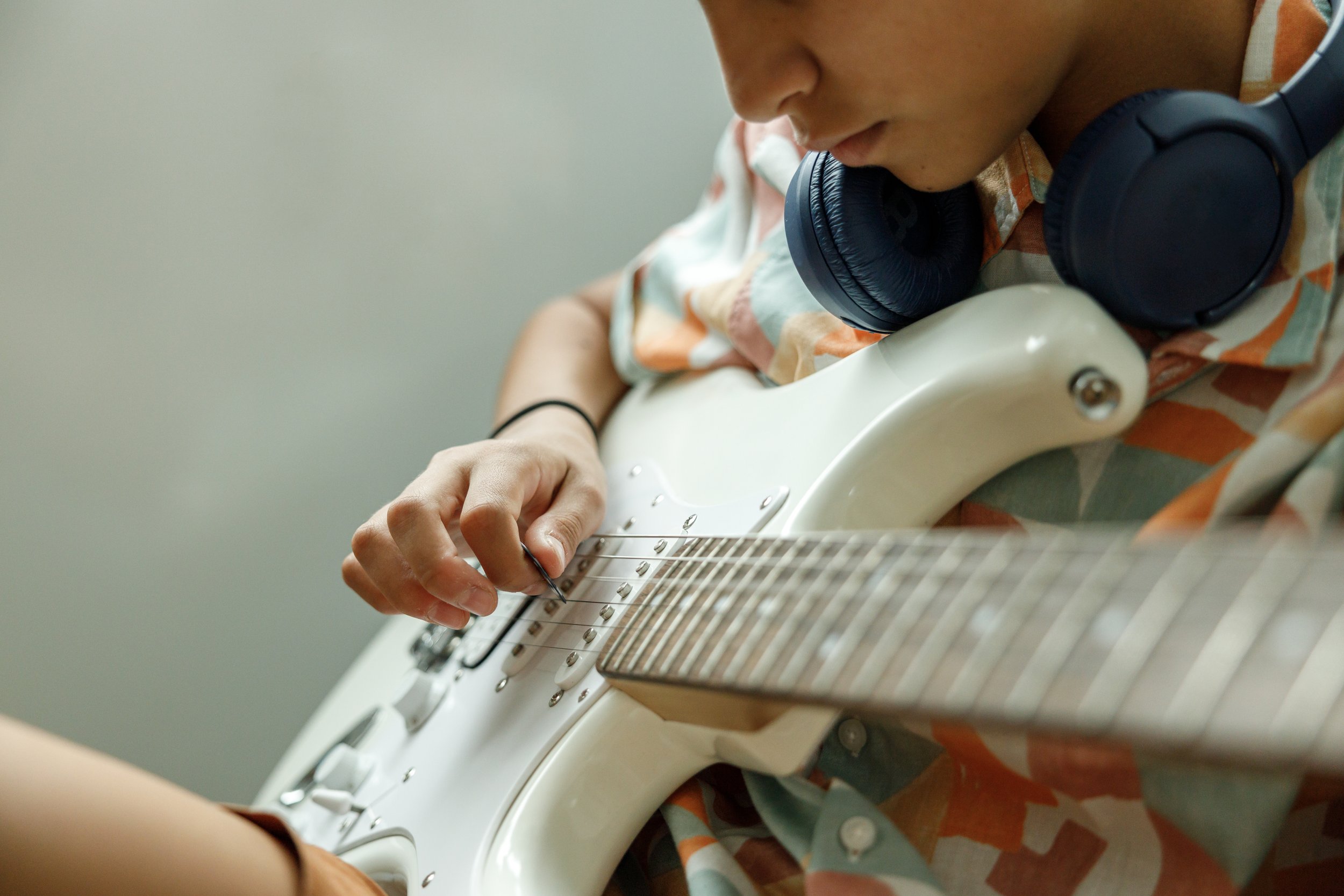 Close-up of a person wearing a colorful shirt, listening to headphones around their neck, playing an electric guitar.