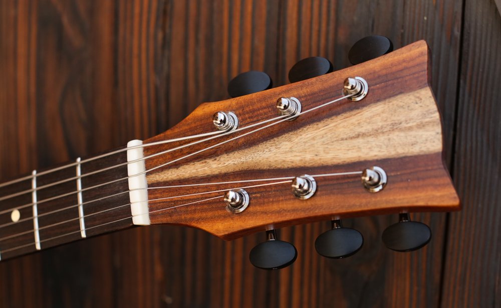 Close-up of an acoustic guitar headstock with tuning pegs against a wooden background.