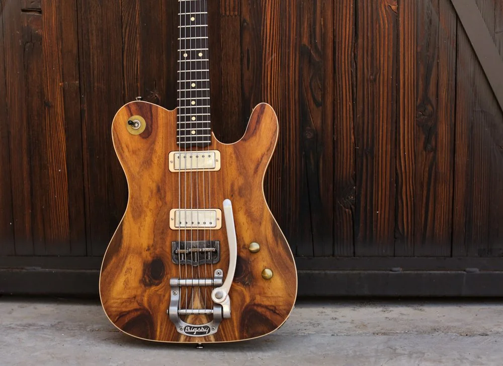 A vintage-style electric guitar with a wood grain finish, mounted against a wooden fence.