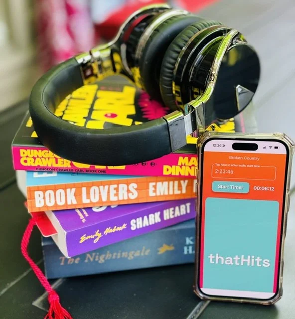 ThatHits audiobook companion app displayed on a smartphone beside headphones and a stack of audiobooks.