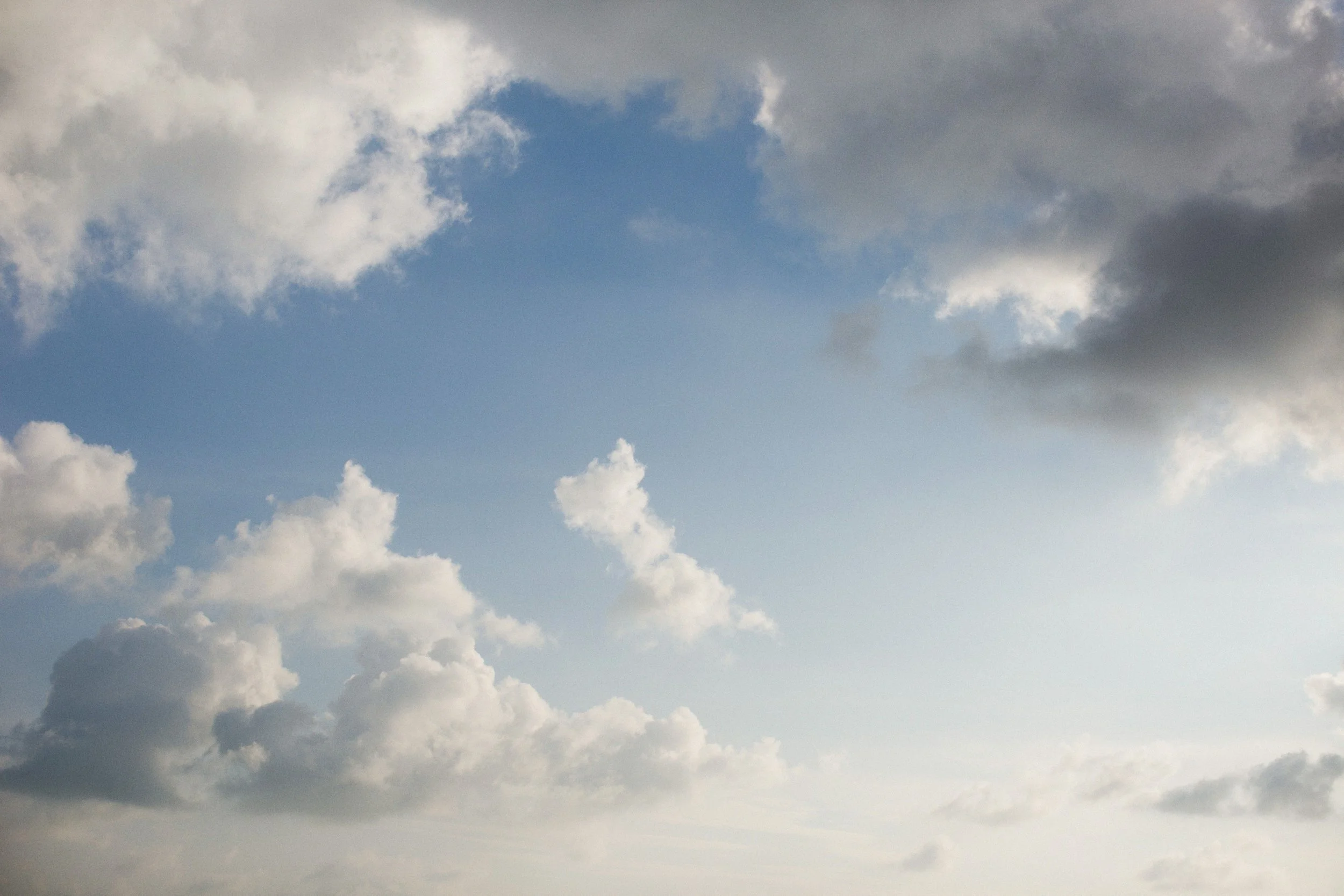 A sky filled with clouds of varying sizes and shades of gray and white, with patches of blue sky visible.