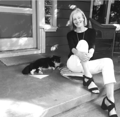 A woman sitting on a porch steps with a black and white cat lying next to her.
