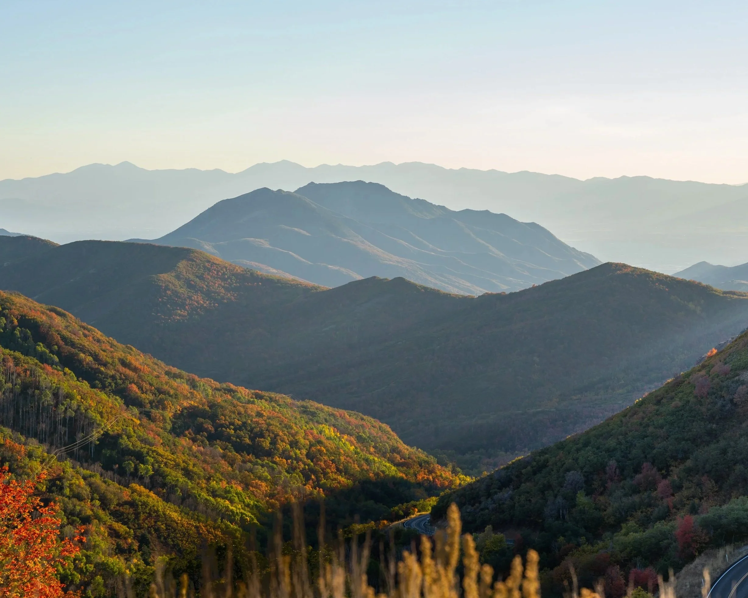 Scenic view of rolling mountains covered with autumn foliage, with distant mountain ranges under a clear sky.