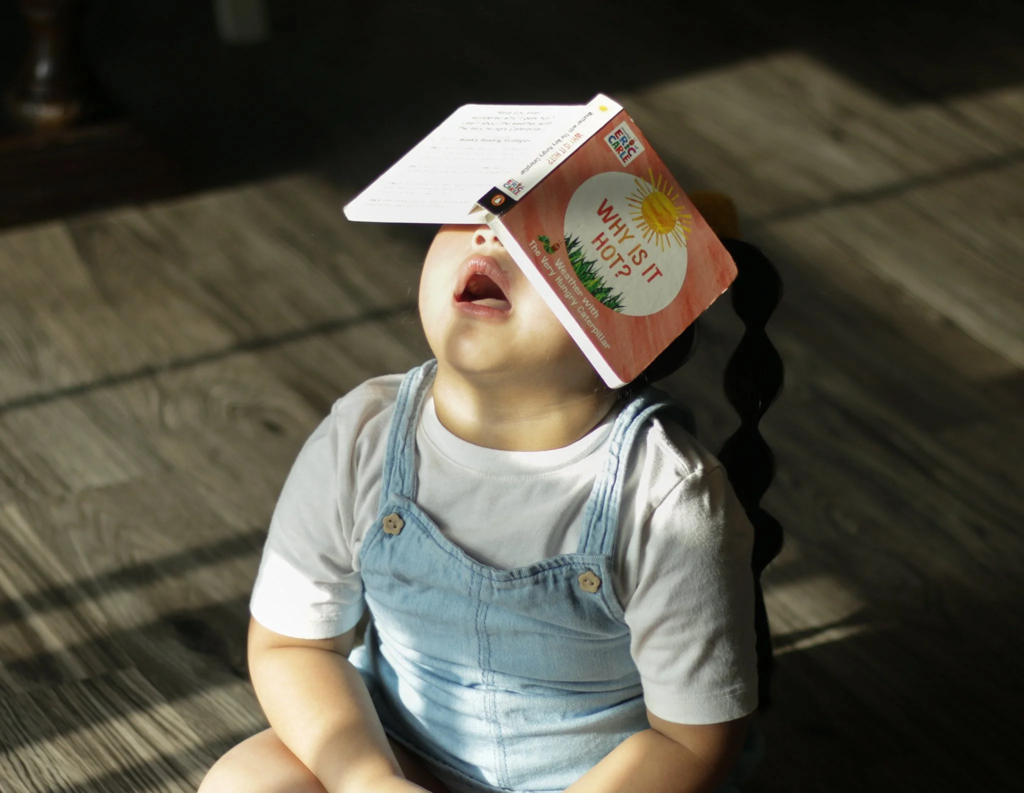 Child holding a juice box with a straw, sitting on a wooden floor.