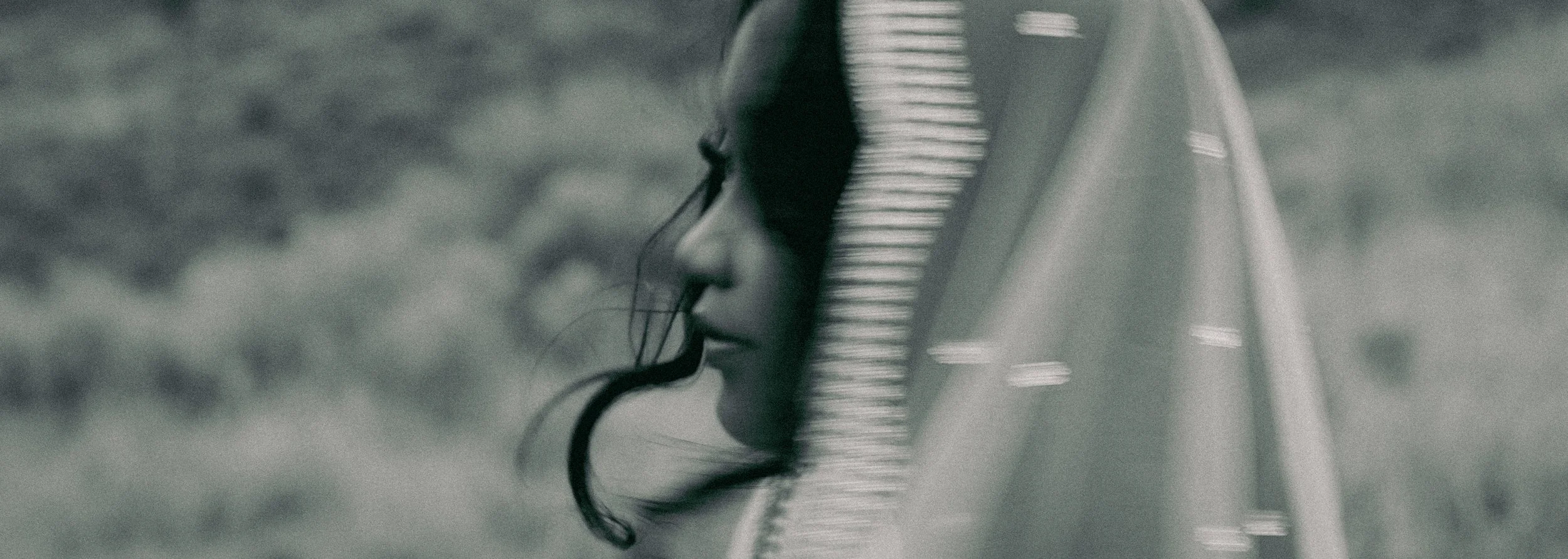 A black and white photograph of a woman with closed eyes, wearing a hood, with her face close to a piano.
