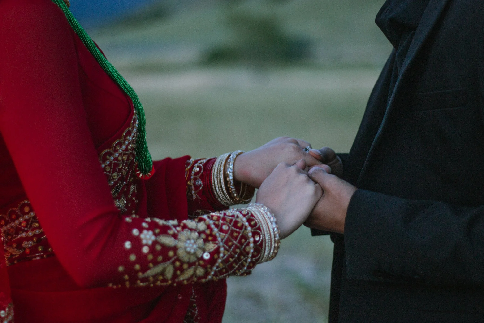 Close-up of a bride and groom holding hands during a wedding ceremony, with the bride wearing a red embroidered traditional dress.