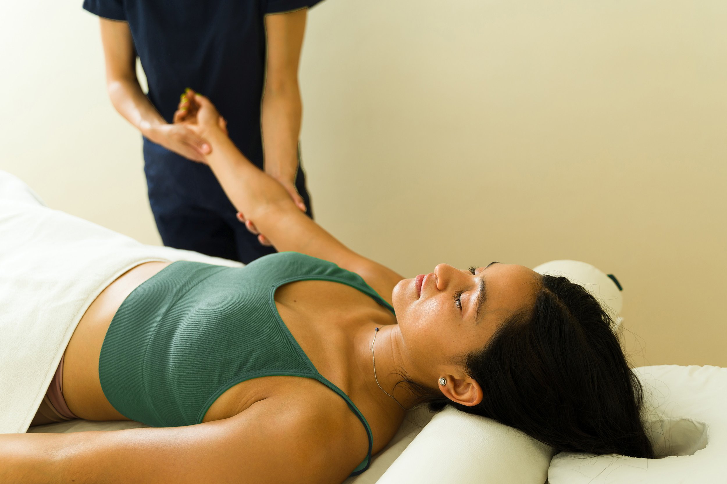 Woman in teal tank top getting a hand massage from a woman in a navy blue scrubs.