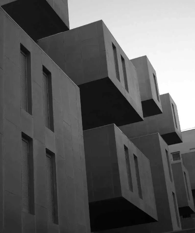 Edificio moderno de varias plantas con balcones en forma de cajas y ventanas estrechas, en una imagen en blanco y negro.