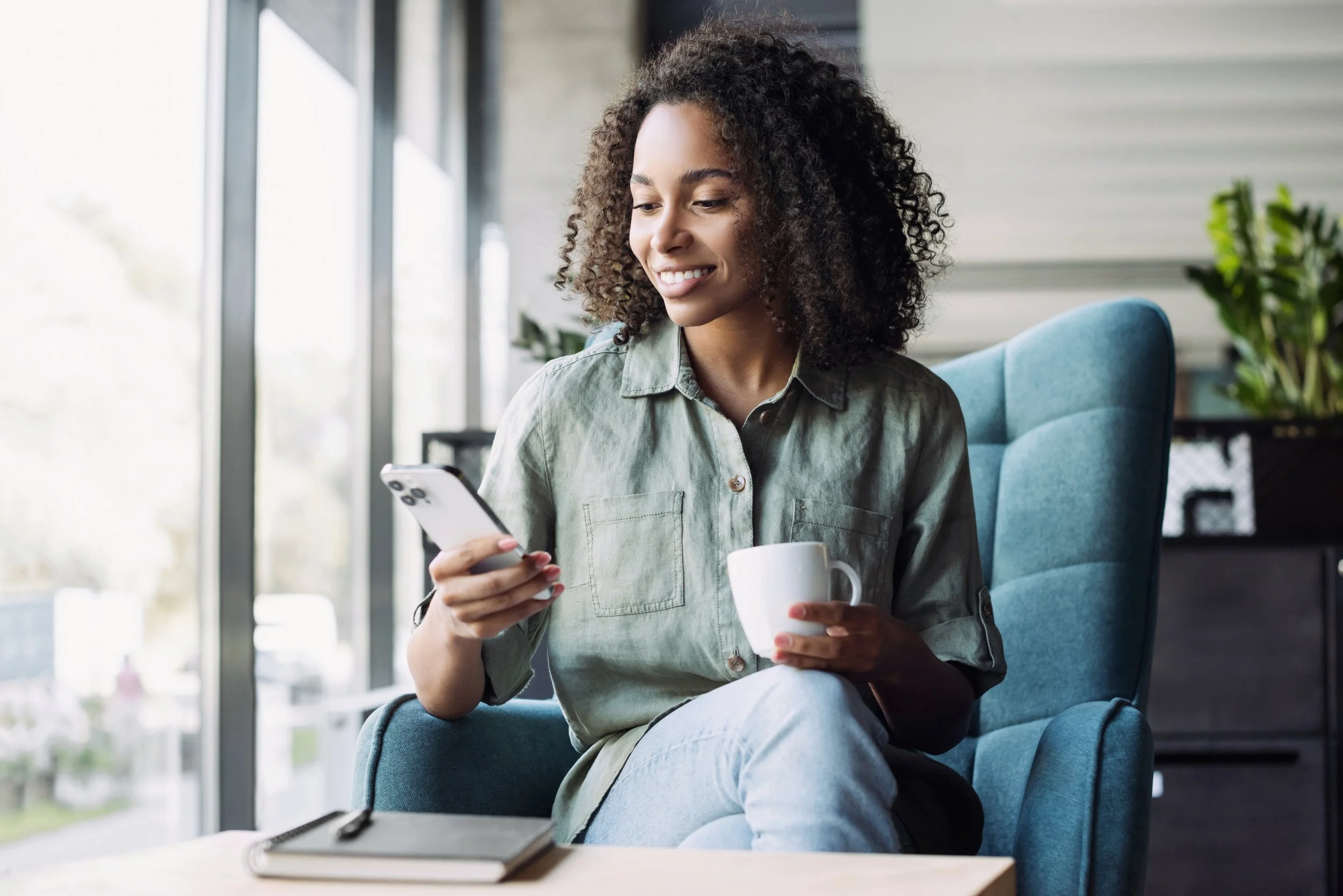 woman sitting in a teal chair texting on an iphone