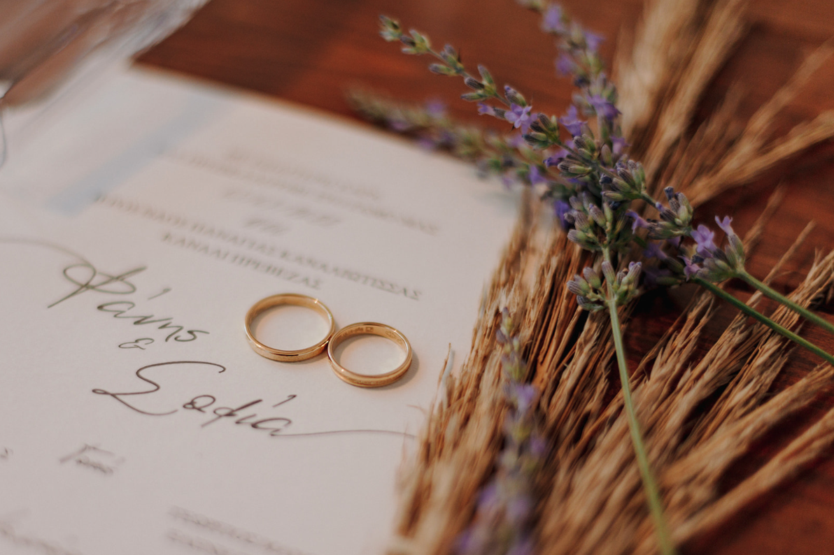 Pair of gold wedding rings placed on a wedding invitation with dried lavender flowers nearby.
