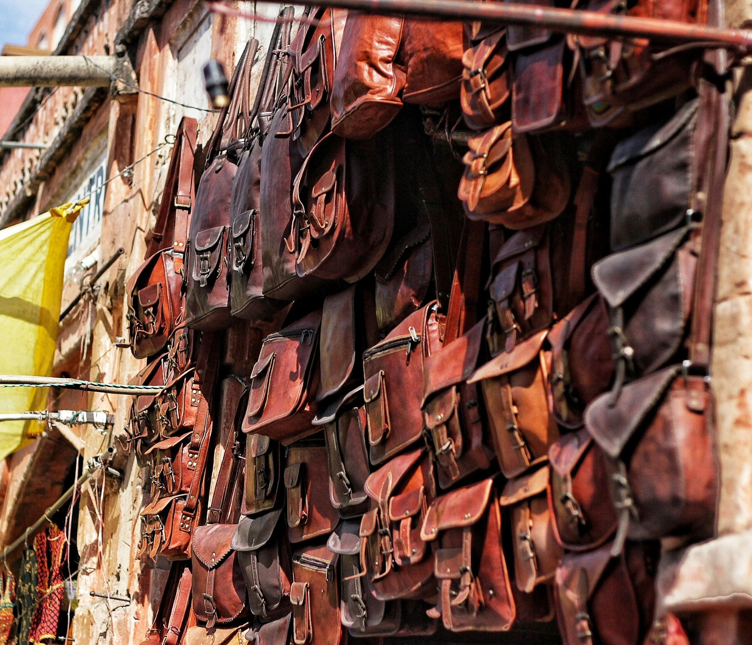 Rows of brown and black leather handbags hanging on a display wall at an outdoor market.